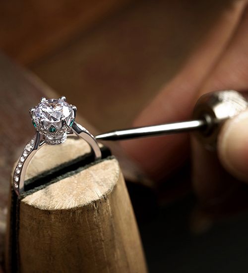 Diamond ring being crafted on a jeweler’s workbench with a metal tool.