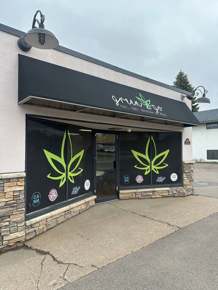 Exterior of a cannabis dispensary, black awning, large green cannabis leaf logos on windows.
