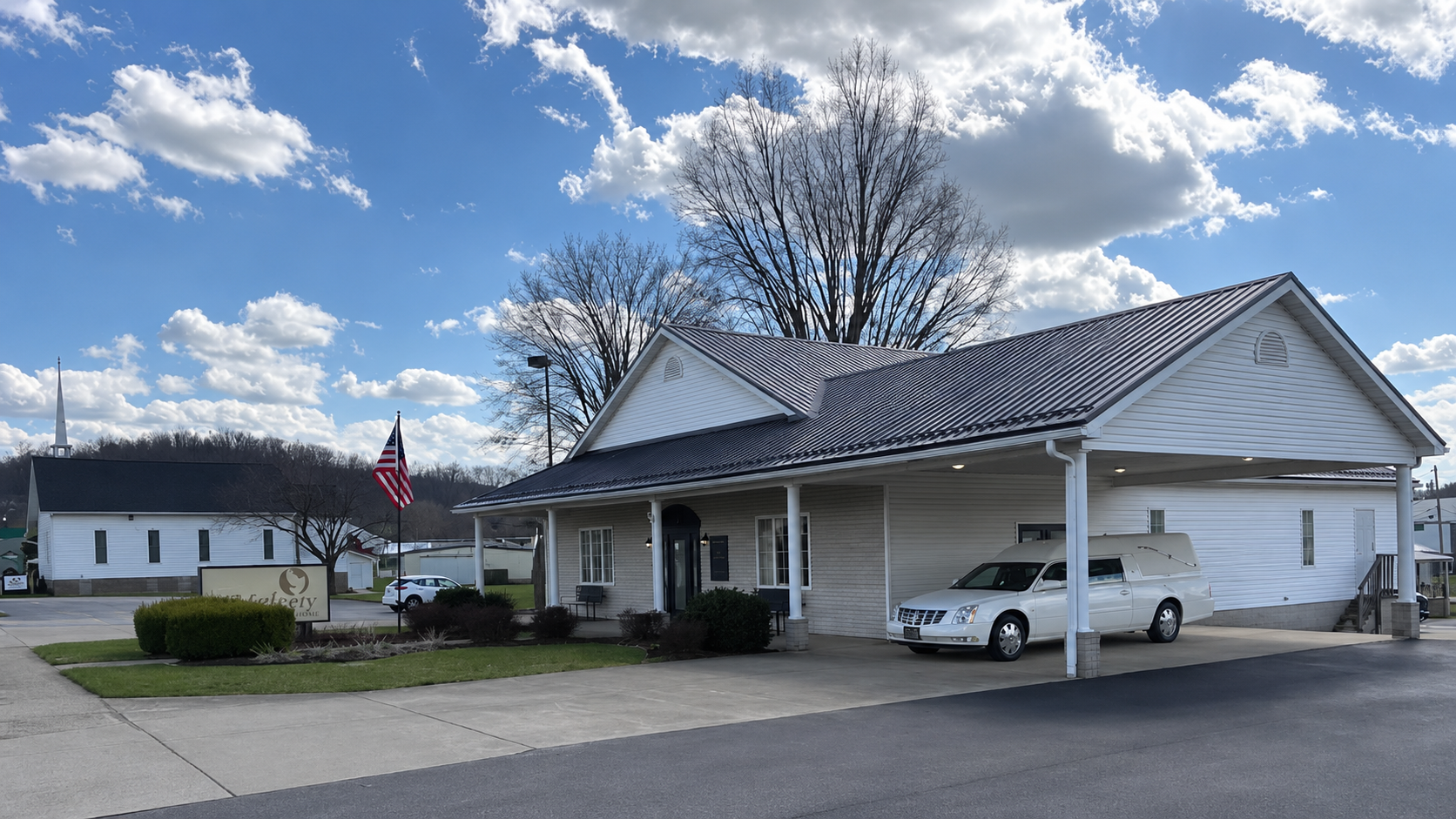White house with carport and parked white pickup under a blue sky with clouds