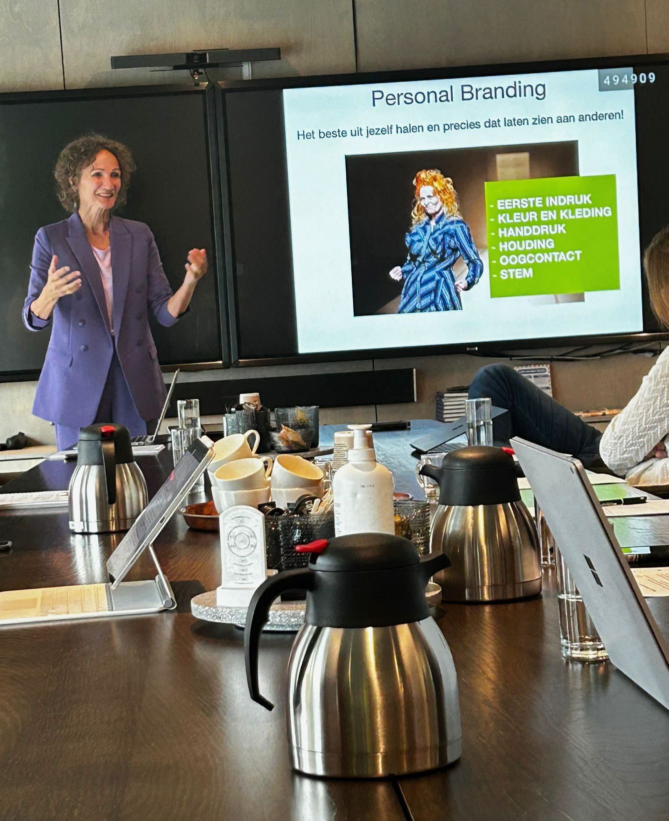 Een spreker in een paarse blazer geeft een presentatie over persoonlijke branding voor een vergadertafel.