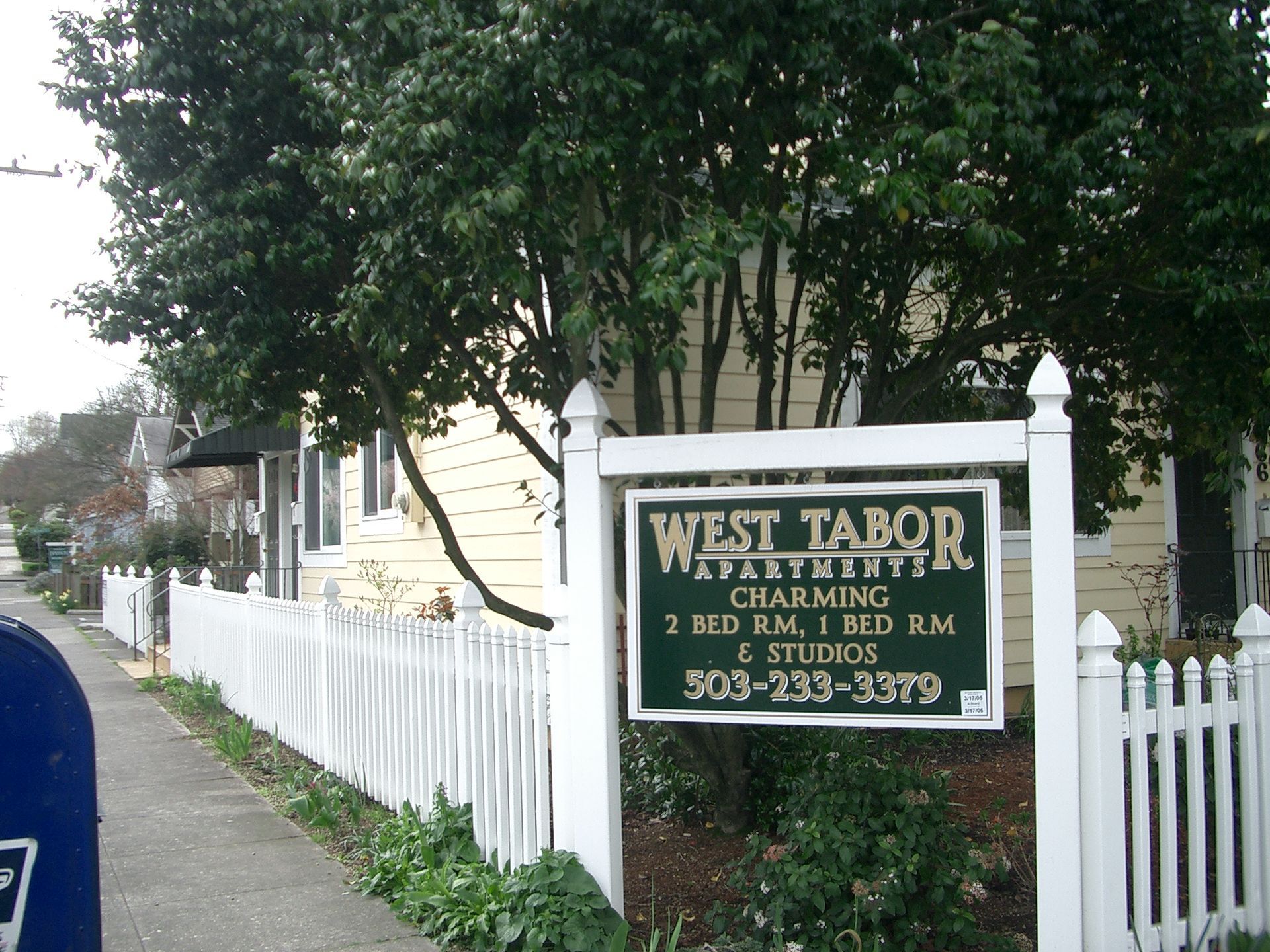 A white picket fence with a sign that says west tabor apartment