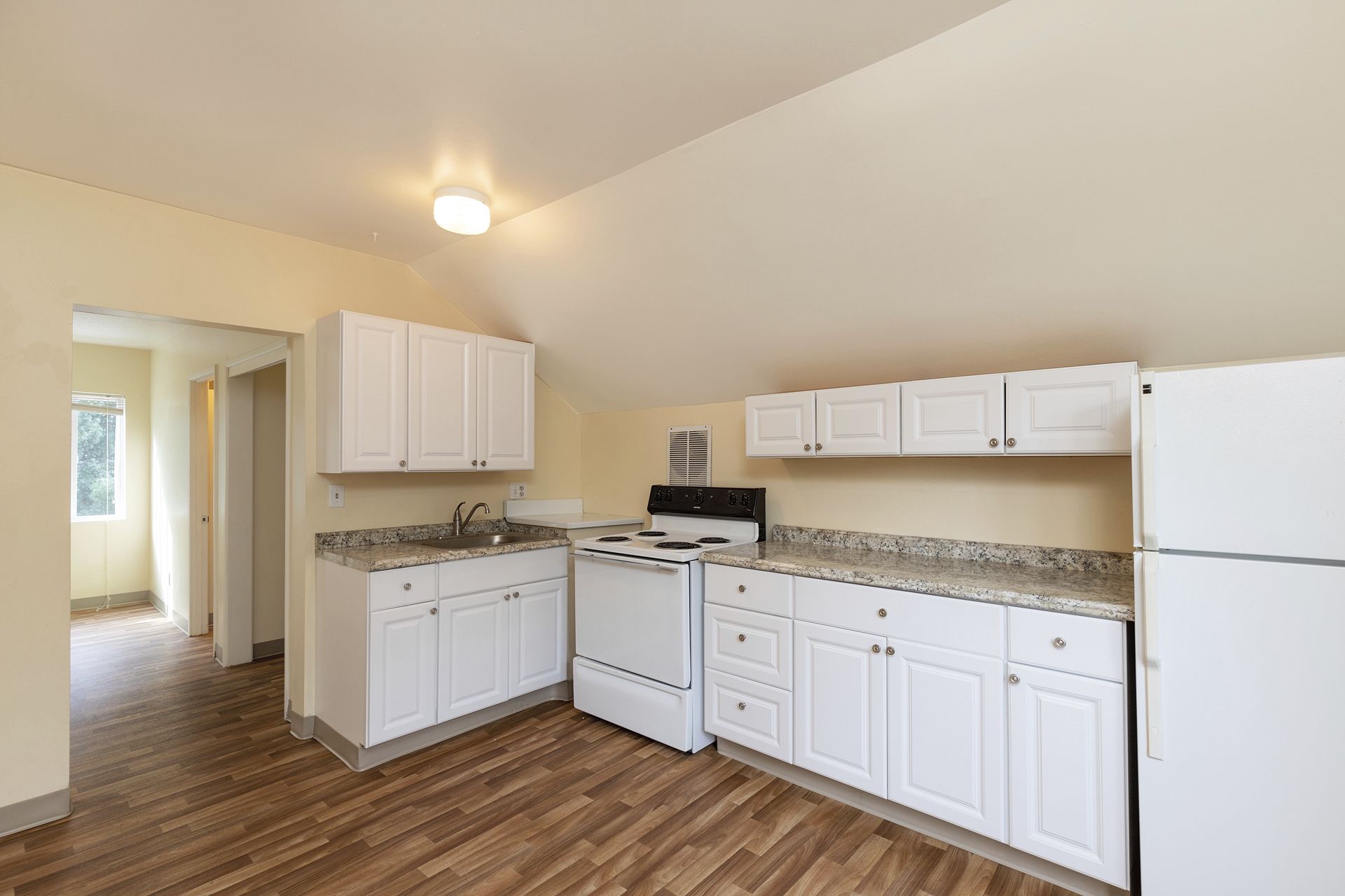 A kitchen with white cabinets , a stove , a refrigerator , and a sink.