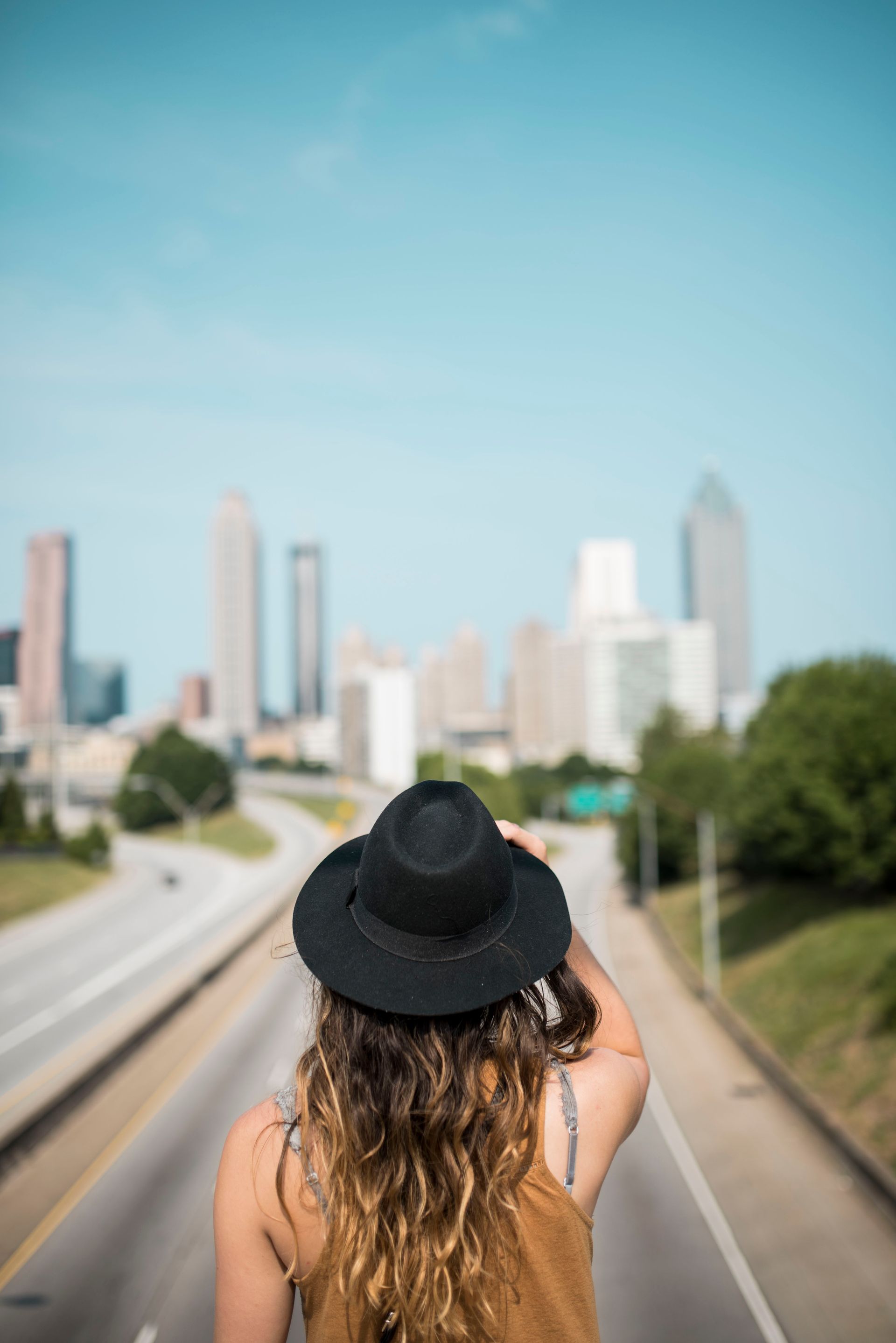 Woman in hat looking at Atlanta skyline from a highway overpass, sunny day.