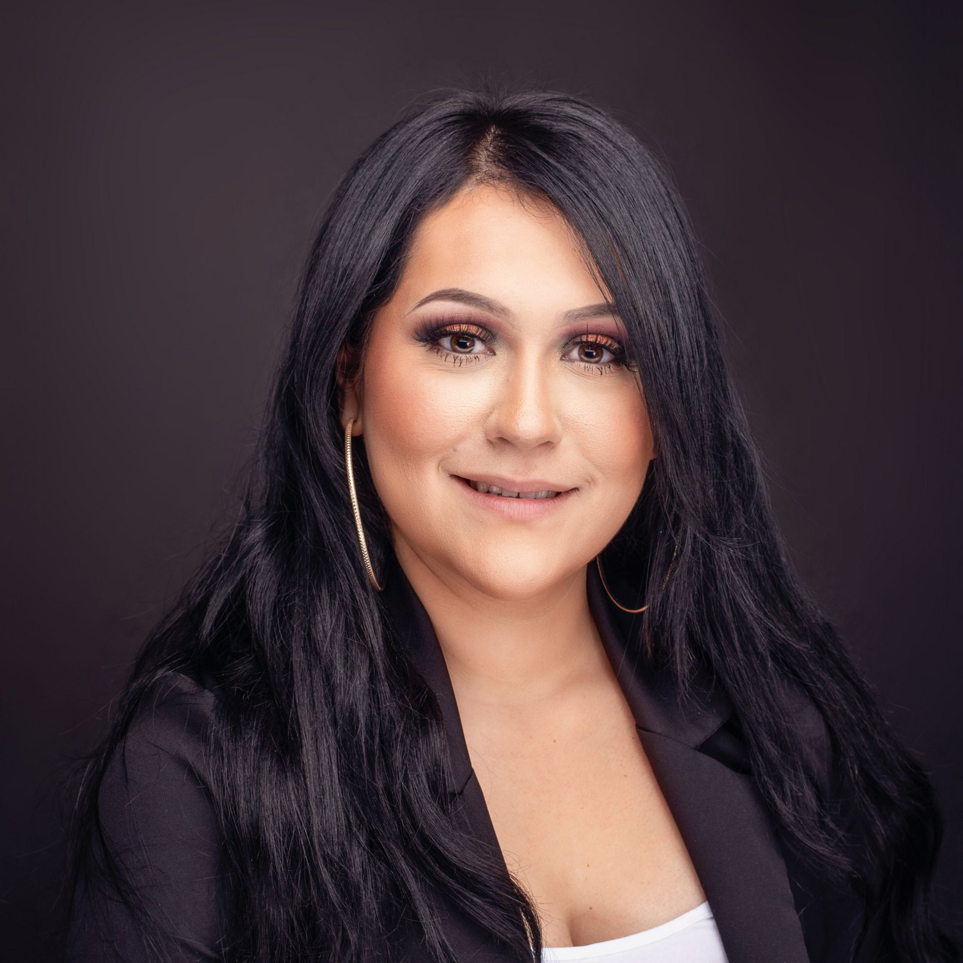 Woman with long dark hair wearing a black blazer, smiling at the camera.