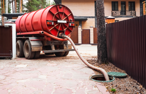 A red vacuum truck is pumping sewage into a manhole cover.