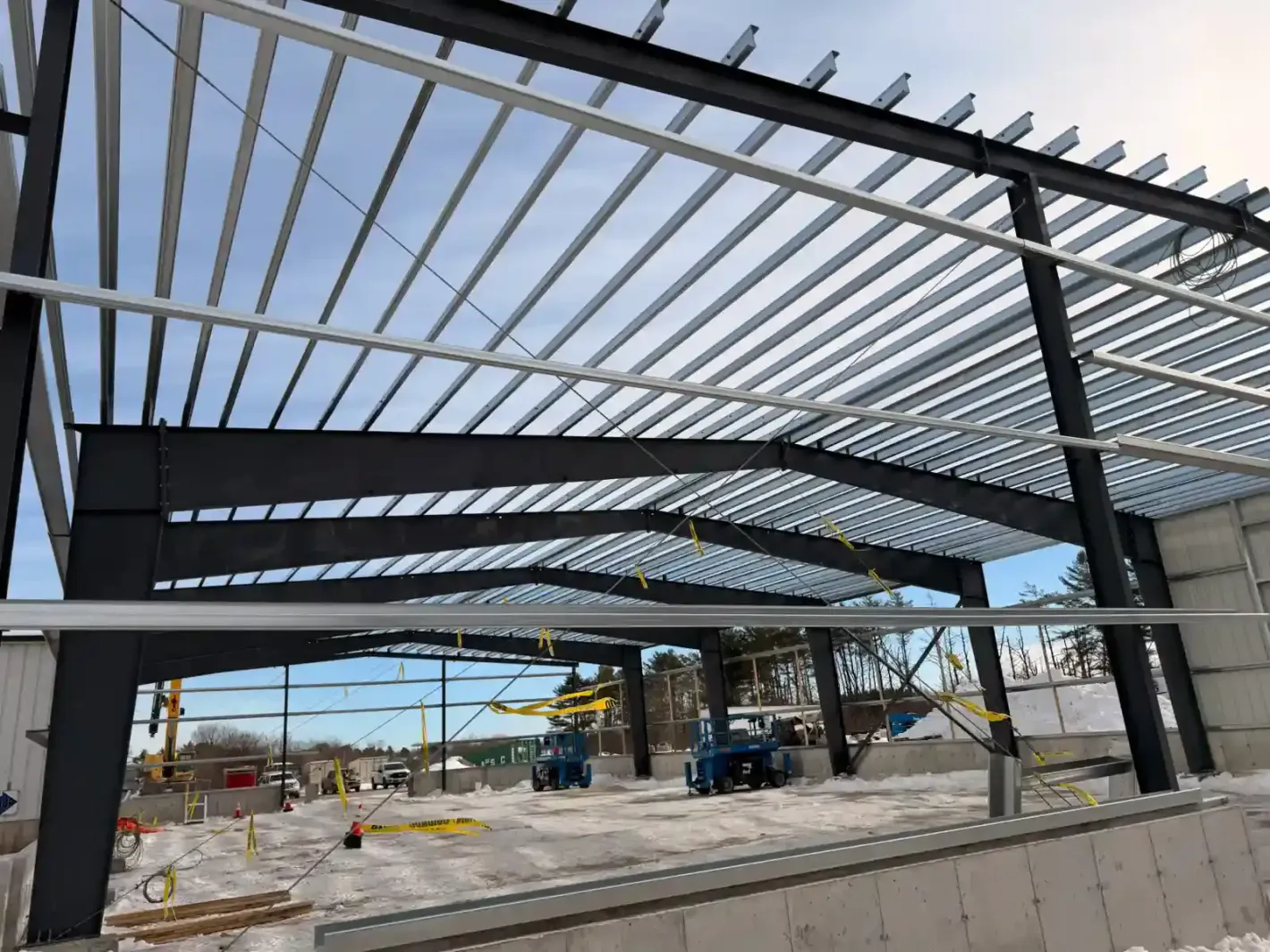Steel framework of a building under construction with workers and equipment on a paved site
