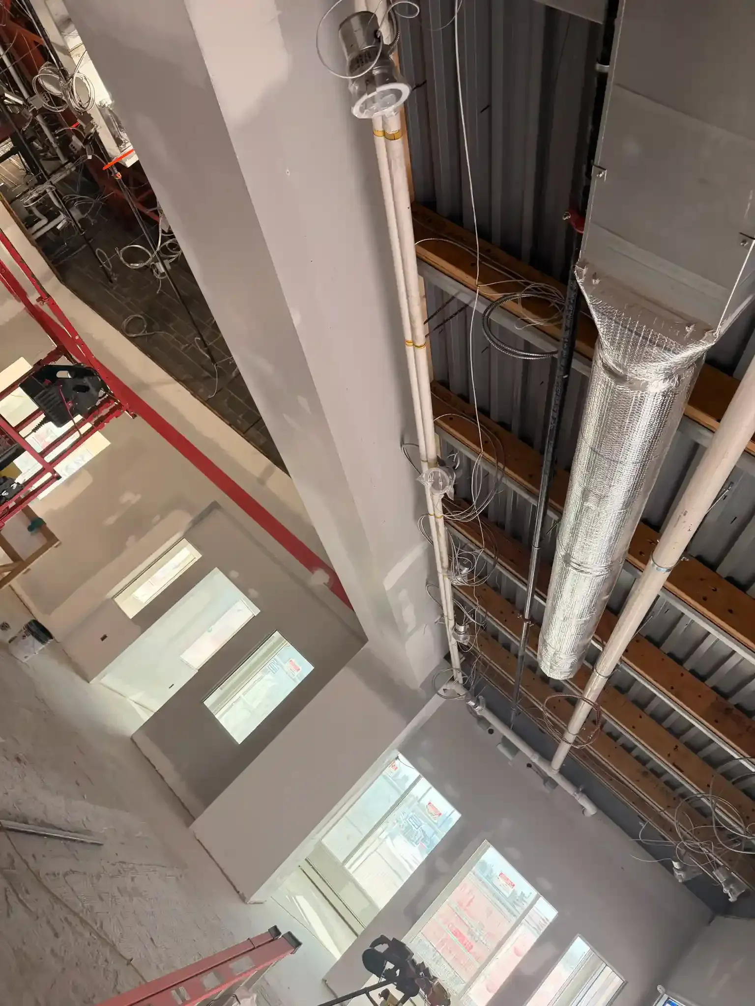 Interior of a building under construction with exposed beams, ductwork, and window openings.