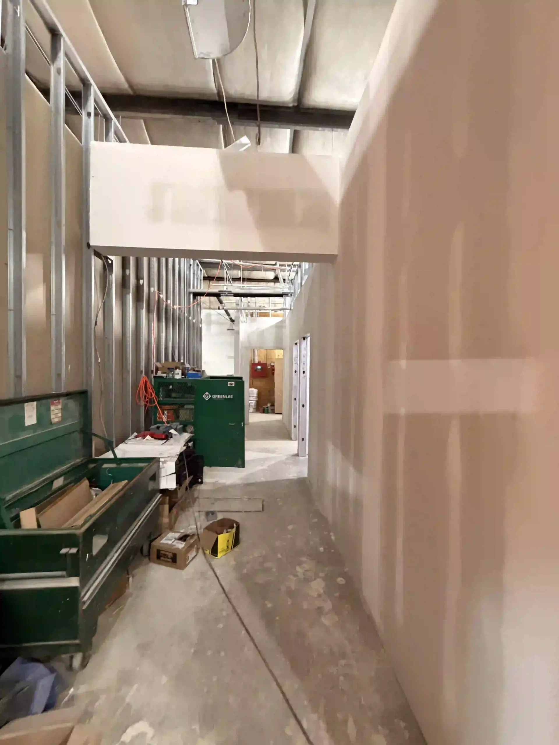 Narrow construction corridor with drywall, tools, and green equipment carts along the left side.