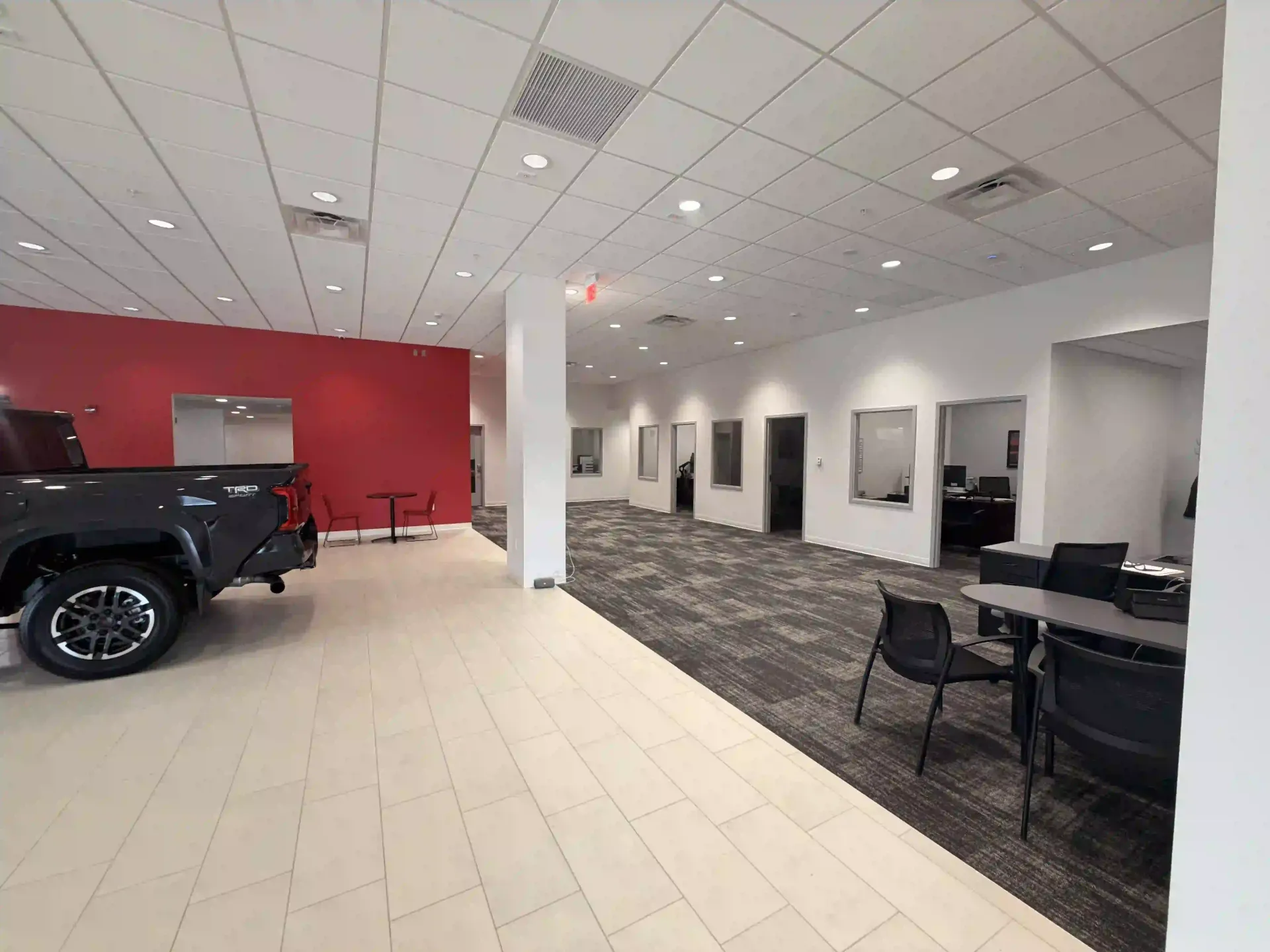 Car showroom with a black SUV, red accent wall, white tile floor, and seating area