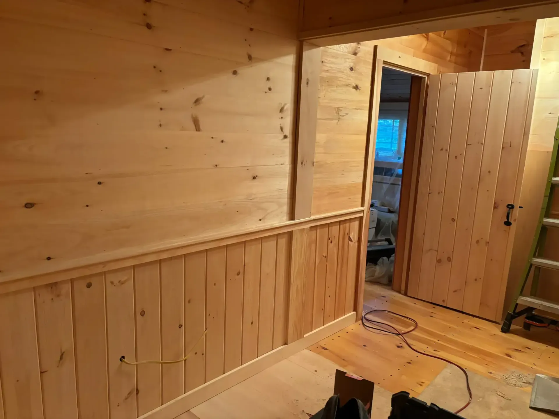 Wood-paneled hallway with open doors and a person’s legs partly visible on the floor.