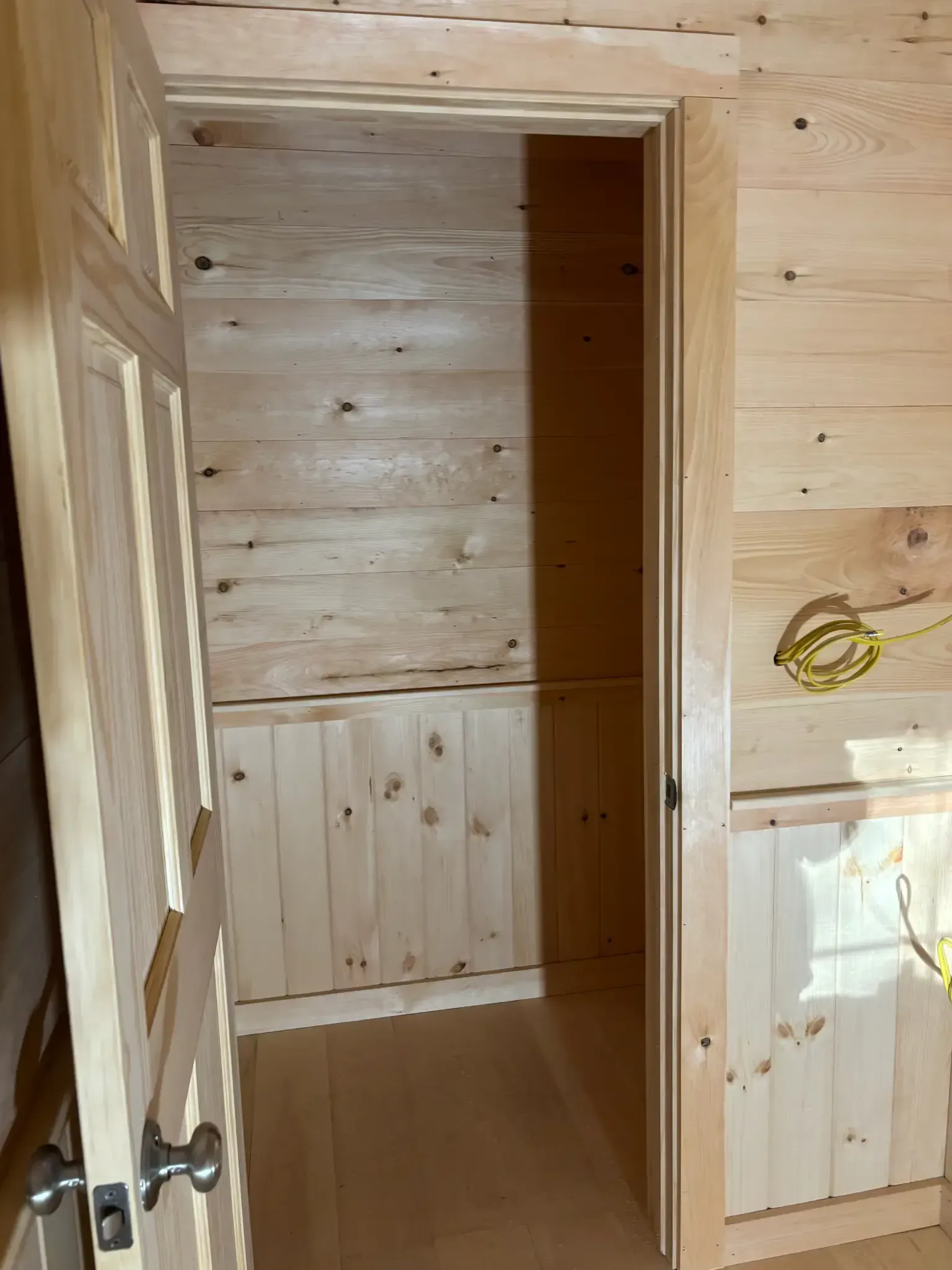 Open wooden doorway to a small unfinished wood-paneled room with a light floor.