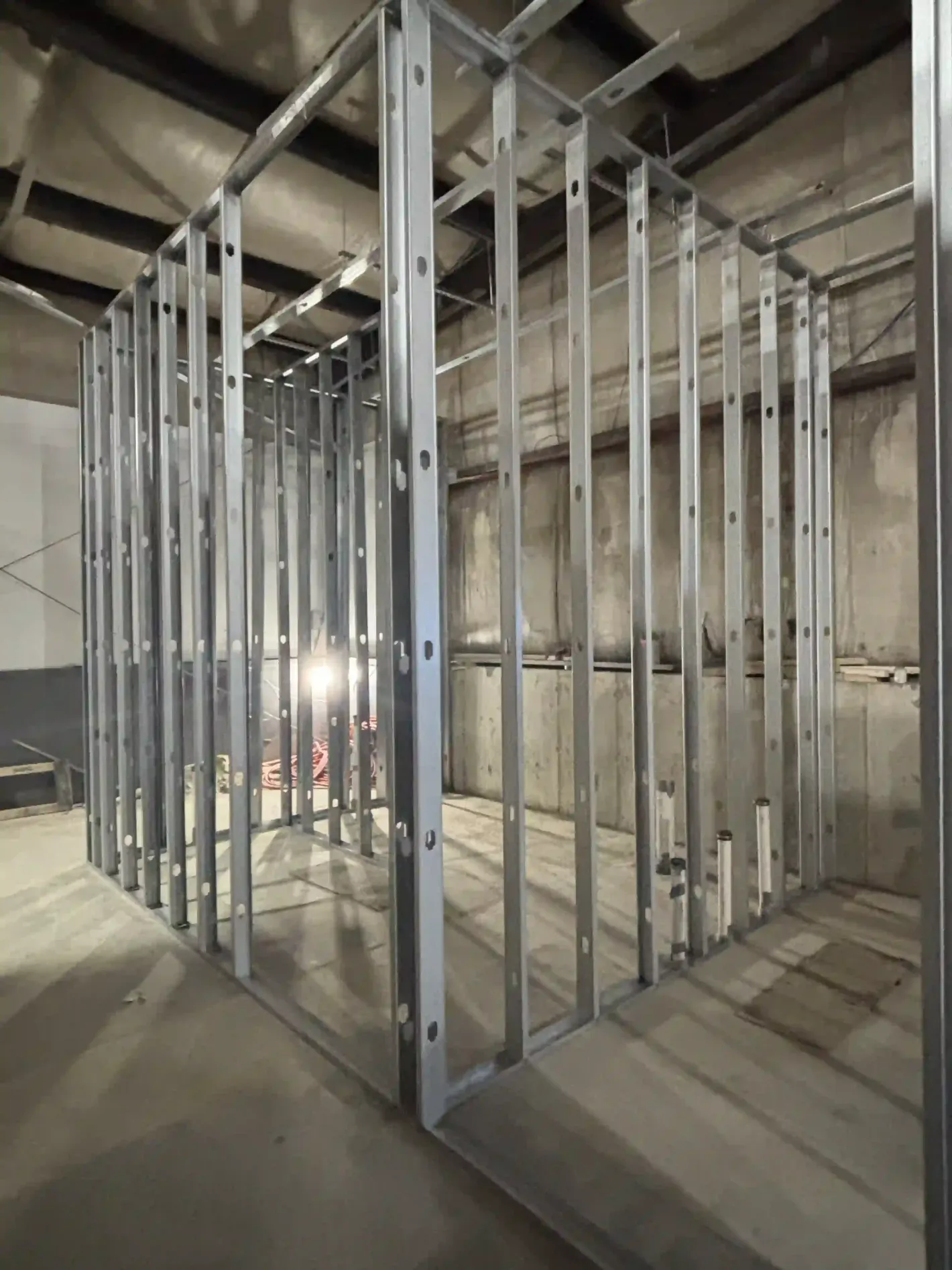 Unfinished building interior with metal wall studs and concrete floors under exposed ceiling beams