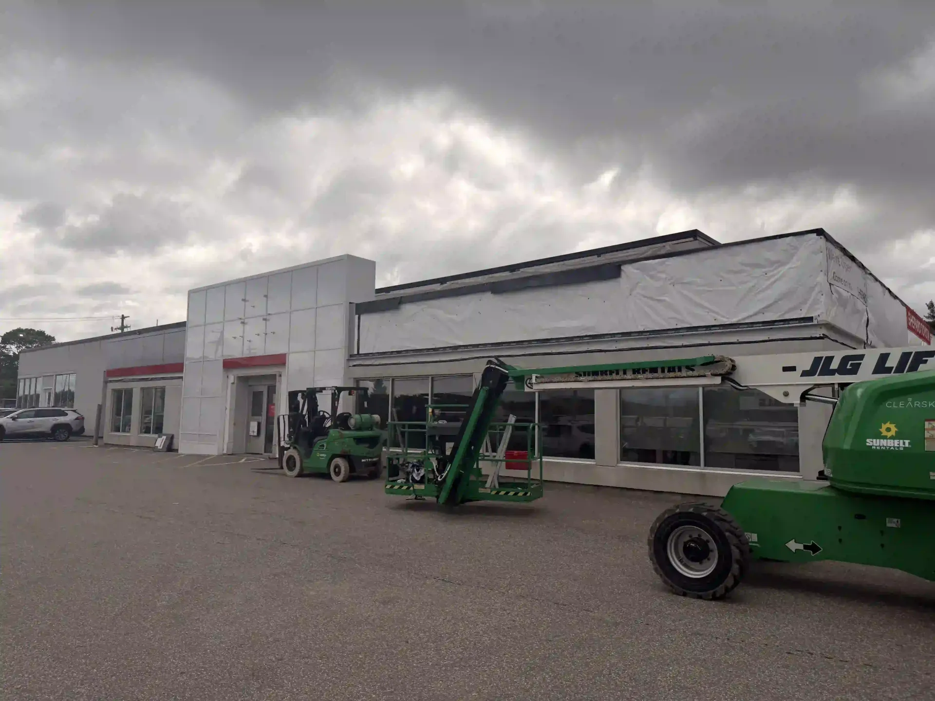Green boom lift and equipment parked outside a commercial building under cloudy skies