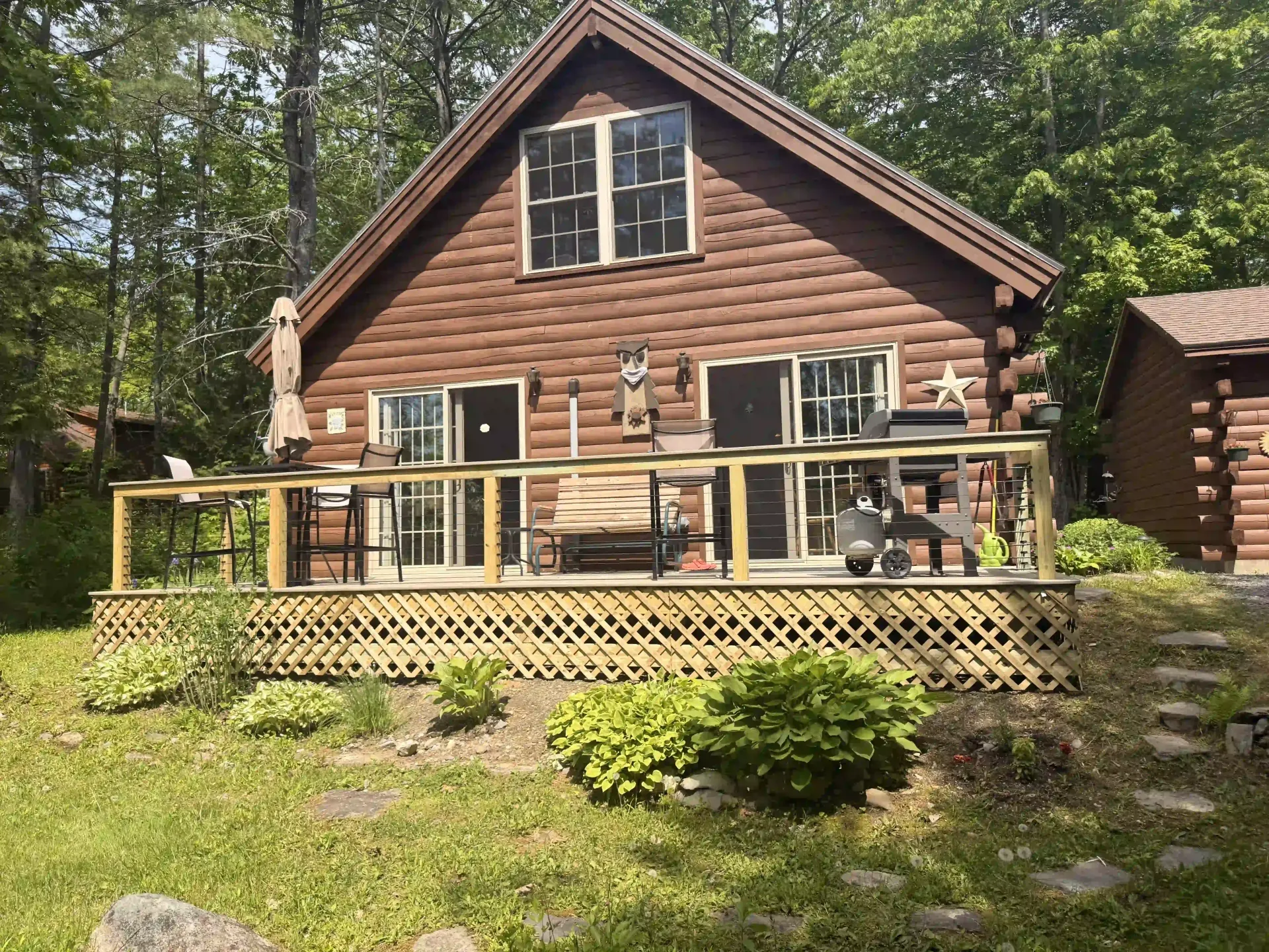 Log cabin with a wooden deck and railing in a wooded backyard