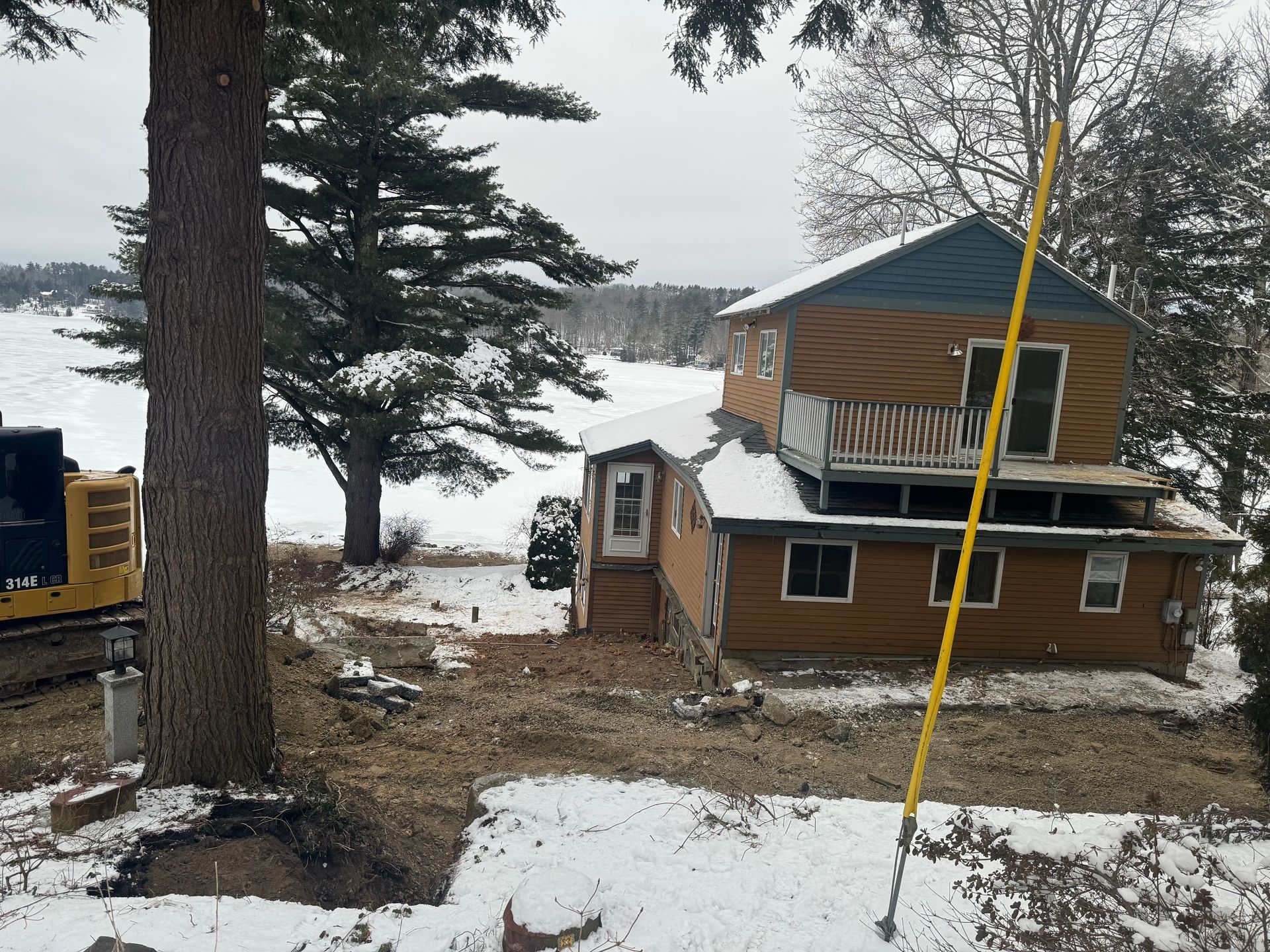 a house with orange siding with a parked excavator next to it in the winter time