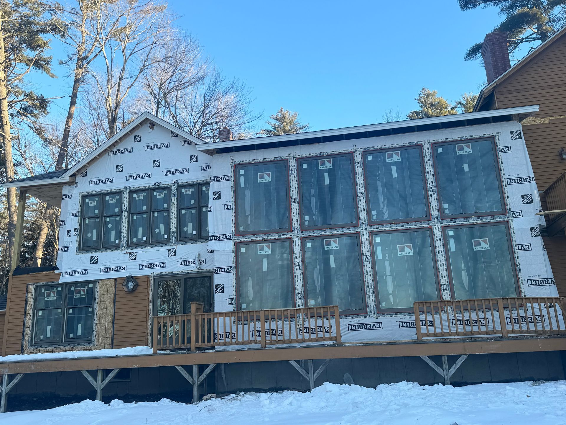 House under construction with blue exterior sheathing and unfinished porch on a snowy day