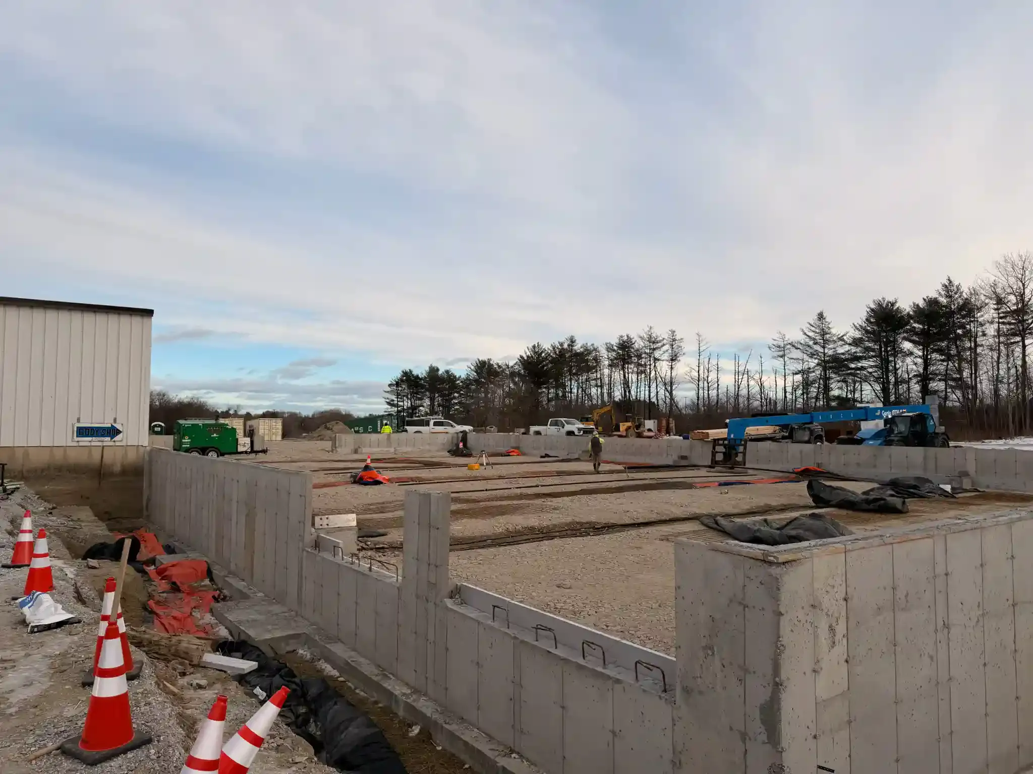 Construction site with concrete foundation walls, orange cones, and equipment under a cloudy sky