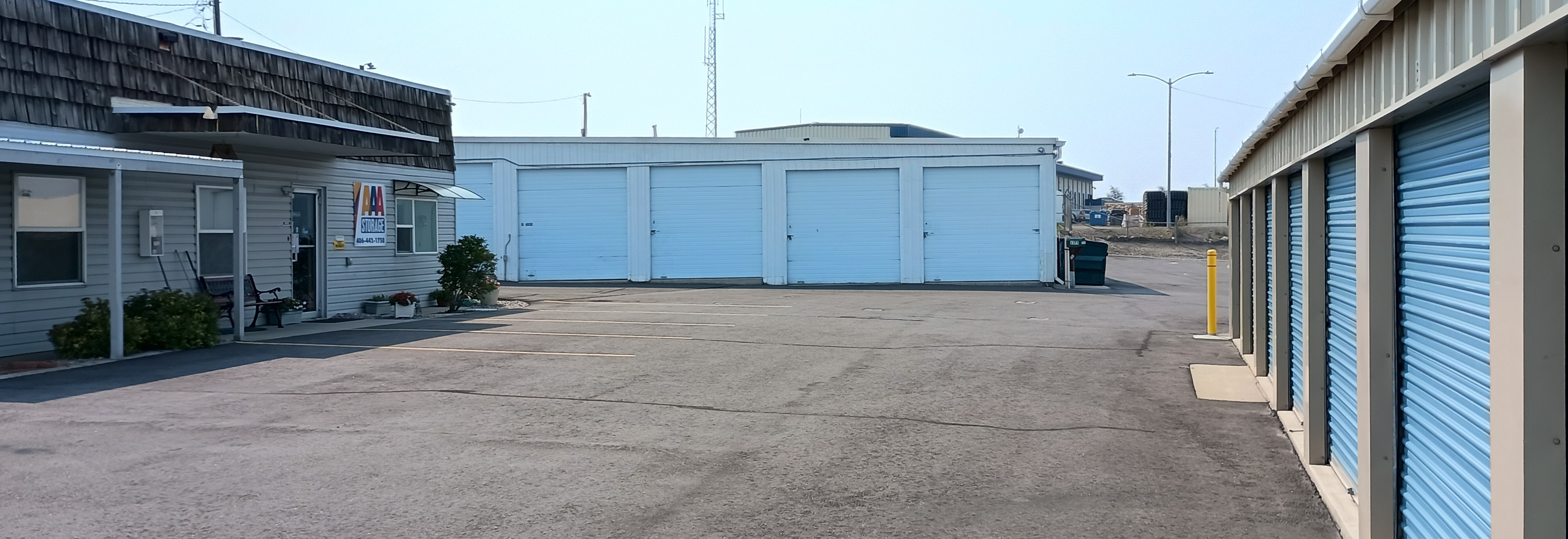 Storage units with white roll-up doors and a blue sign, set against mountains and a cloudy sky.