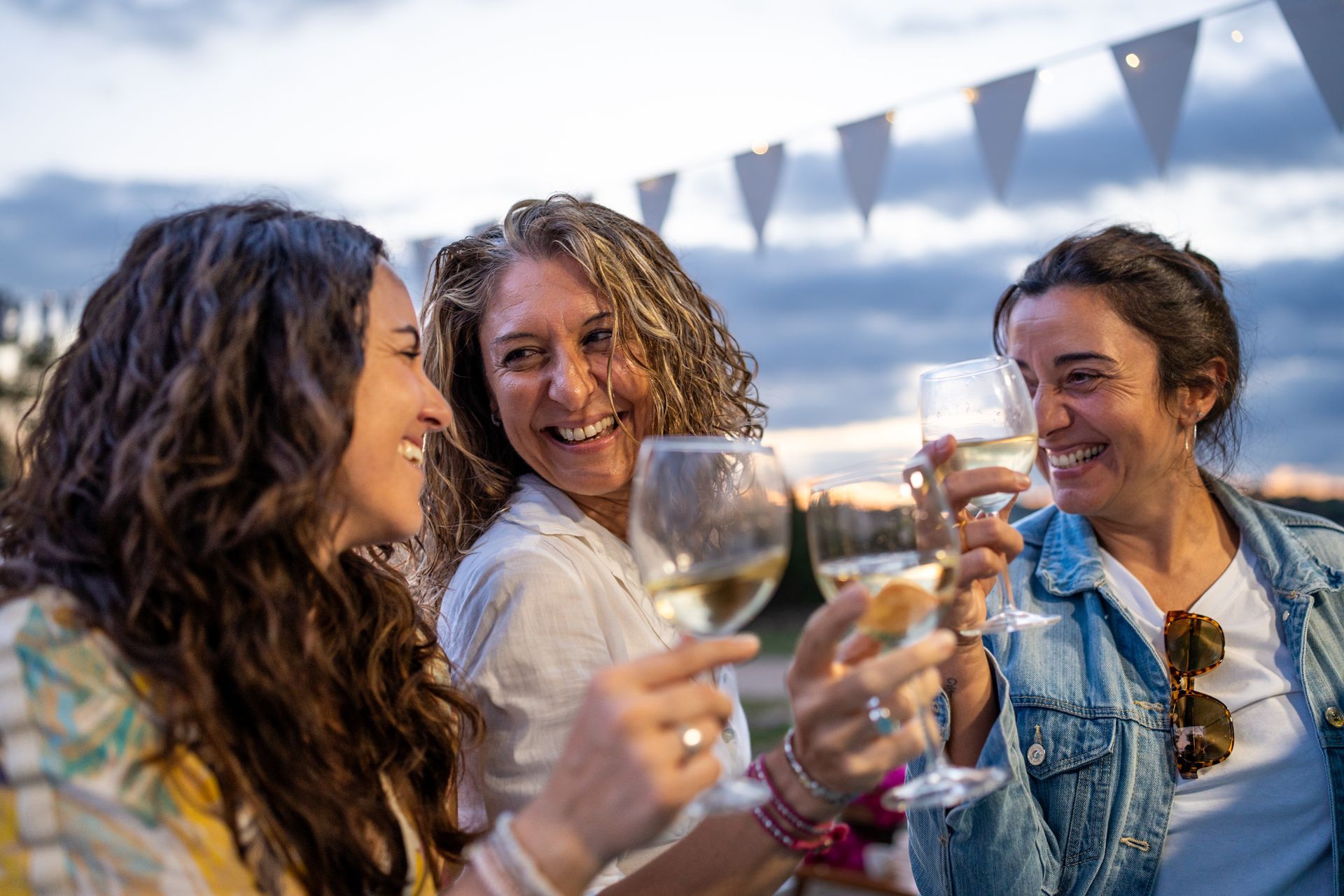 Freunde stoßen bei einer Gartenparty unter Wimpeln mit Weingläsern an und lächeln im warmen Abendlicht.