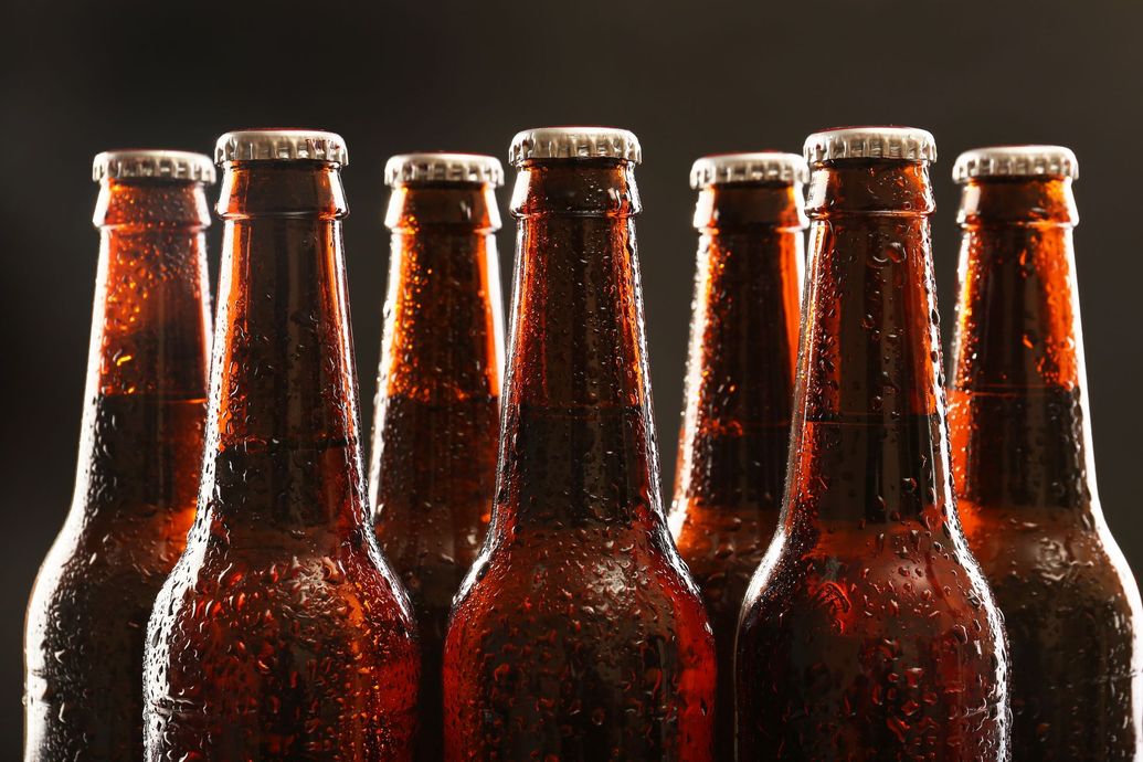 Sechs braune Bierflaschen mit Kondenswasser, aufgereiht vor einem dunklen Hintergrund