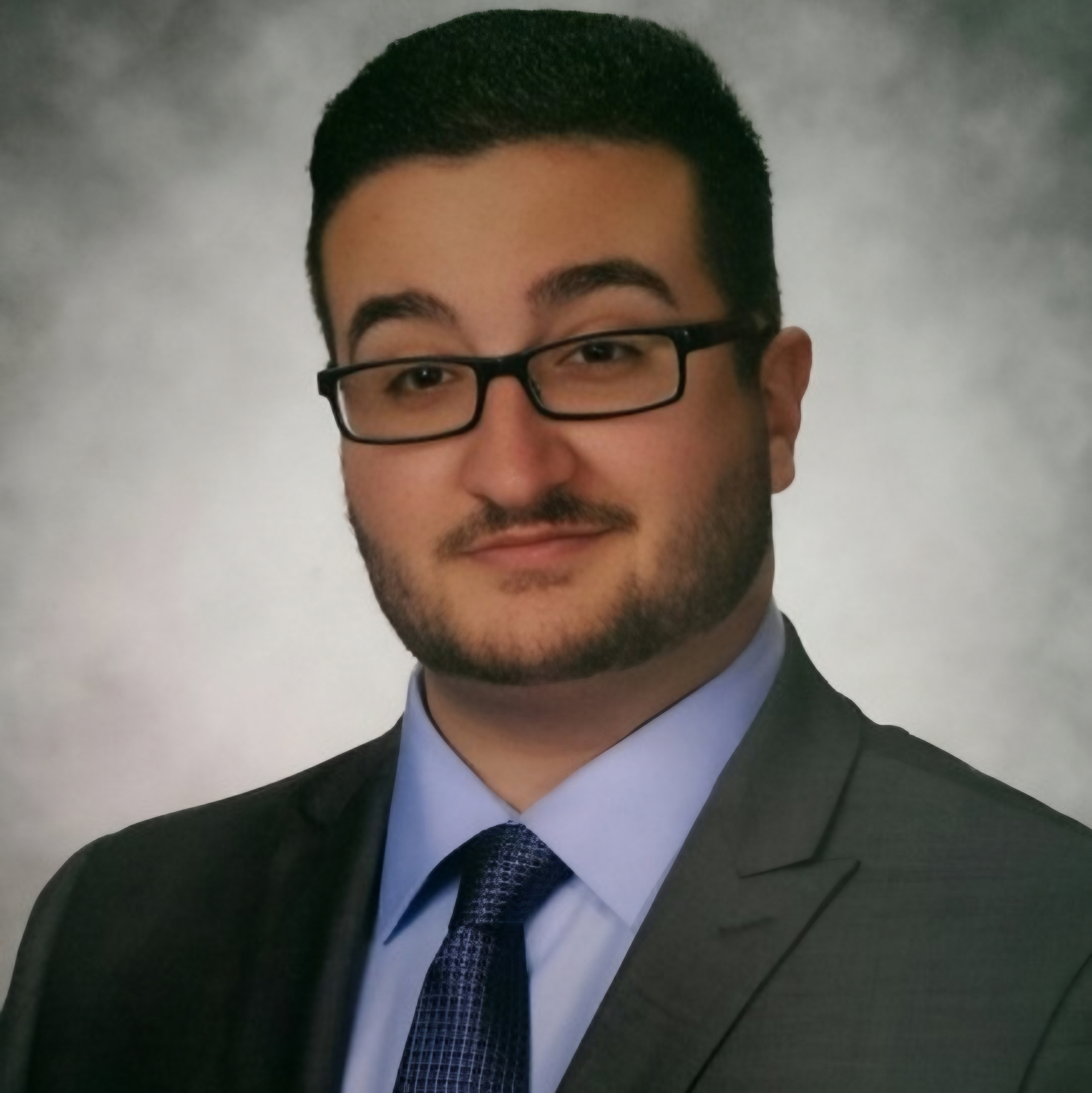 Portrait of a man in glasses and a suit against a gray studio backdrop