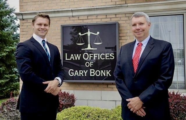 Two men in suits standing outside the Law Offices of Gary Bonk sign