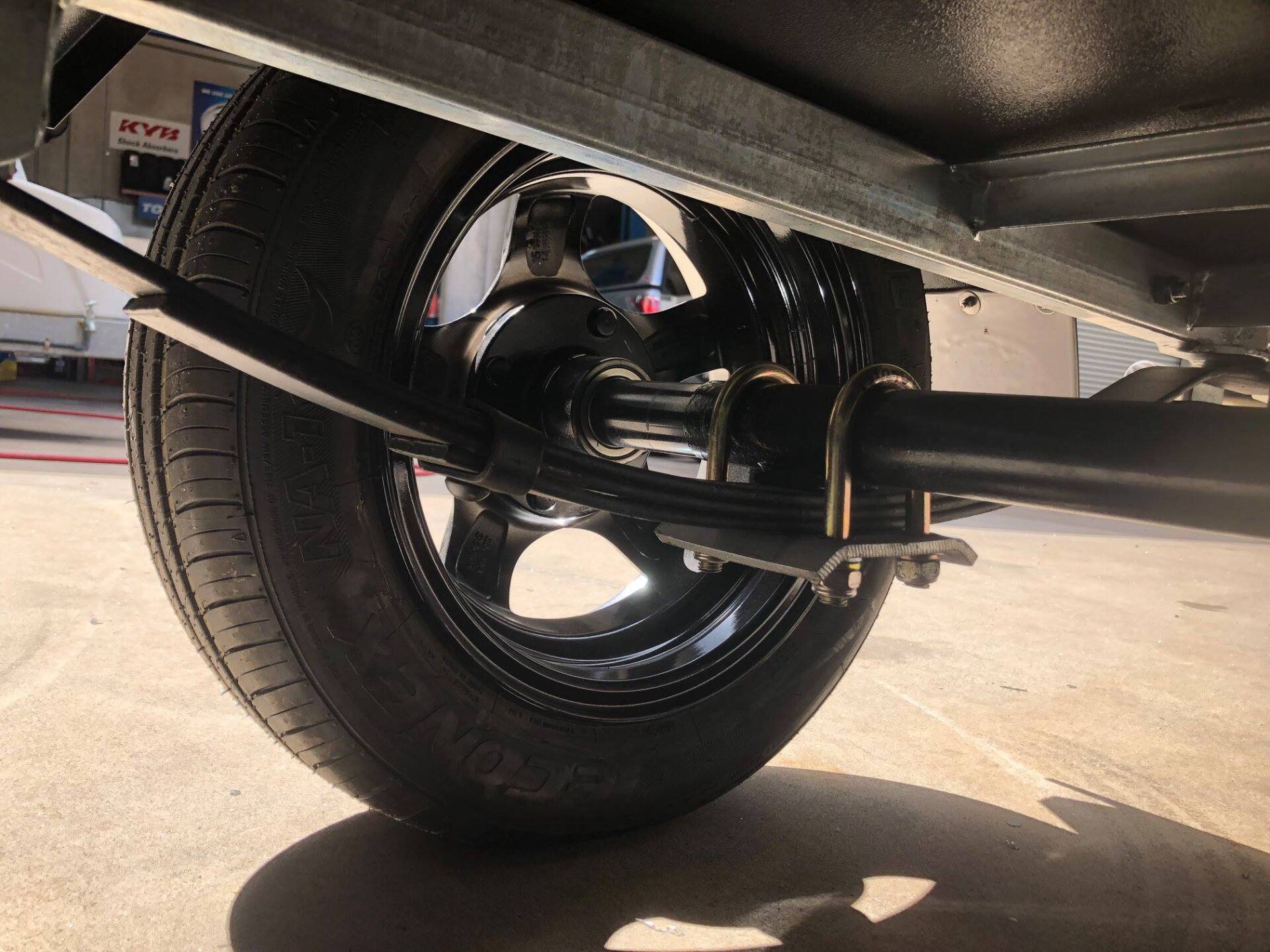 Black trailer wheel with a leaf spring suspension system, viewed from below.
