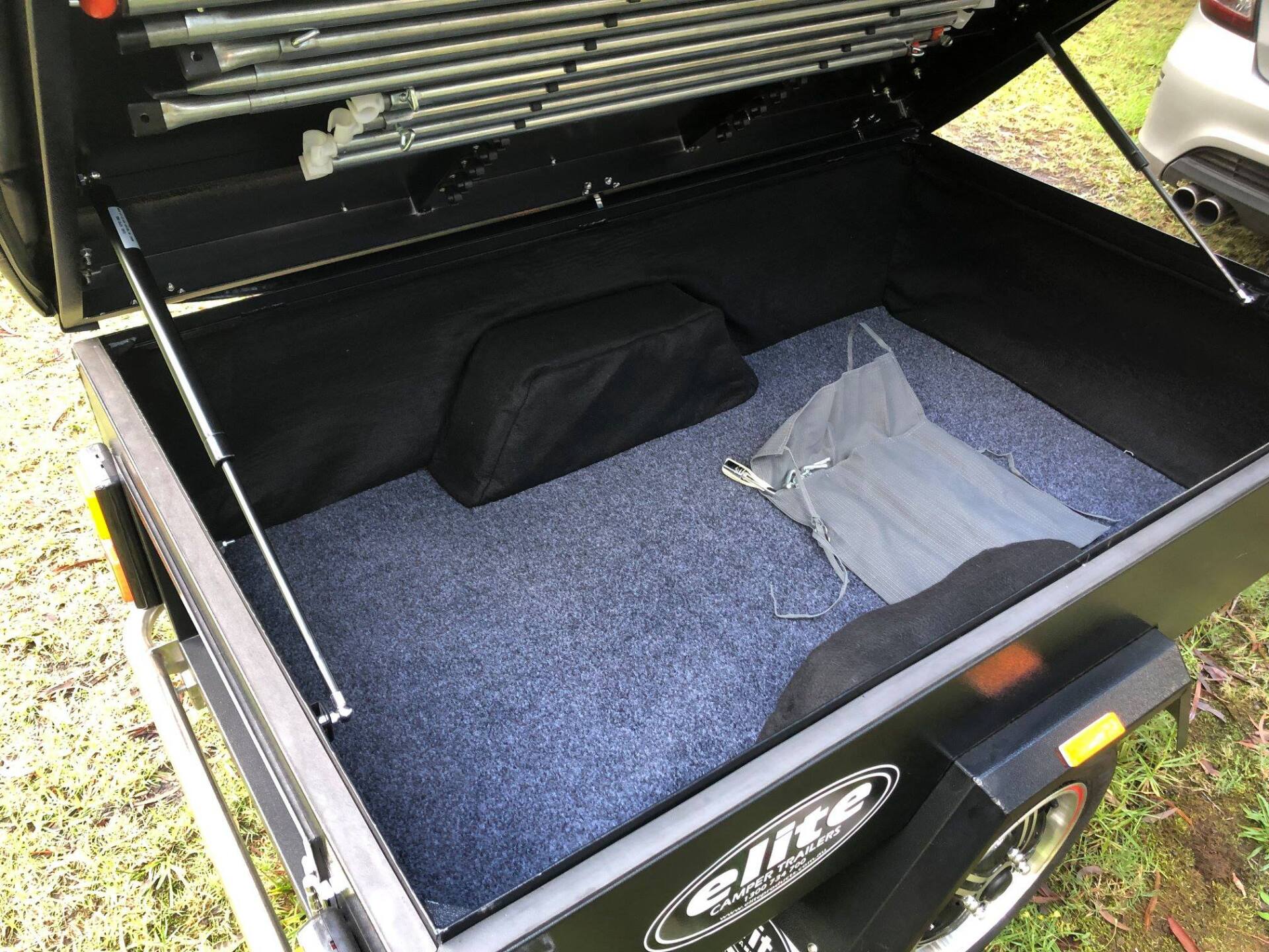 Open trailer bed with a blue carpet, a black bag, and a gray folded tarp.