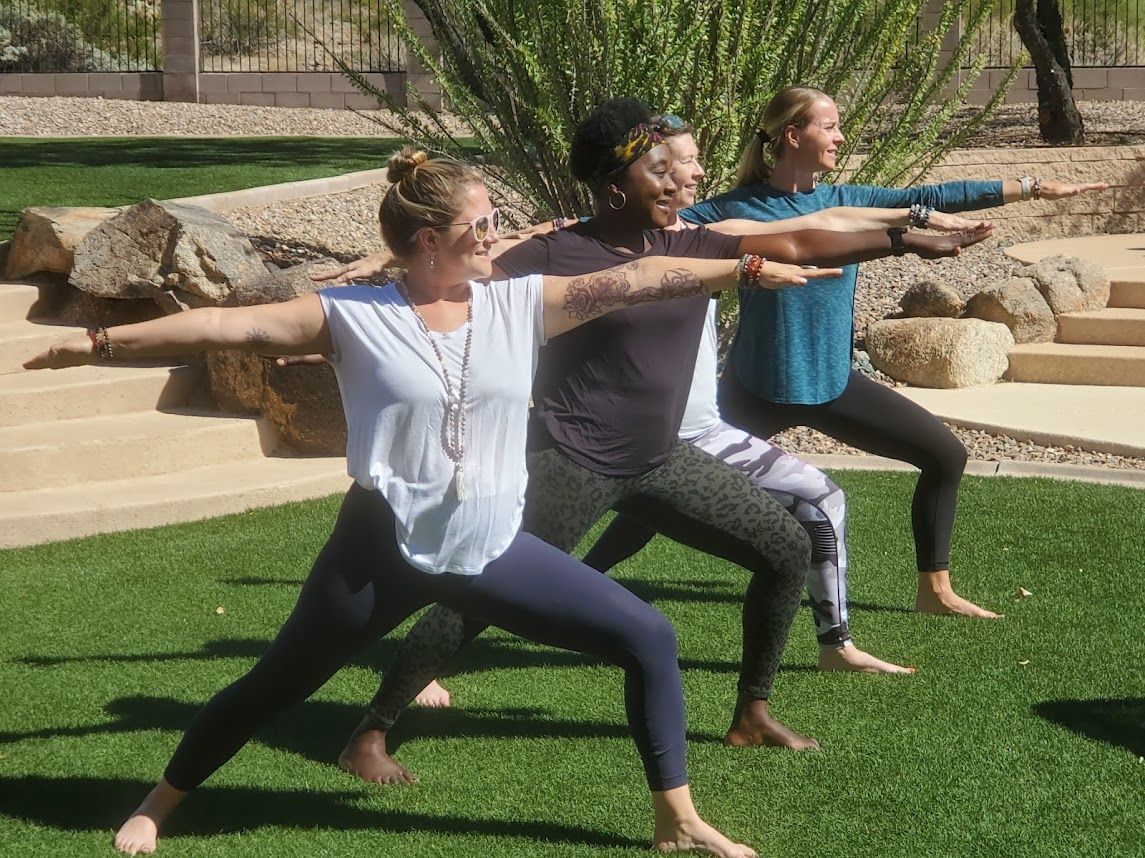 Three people doing yoga pose on green grass outdoors.