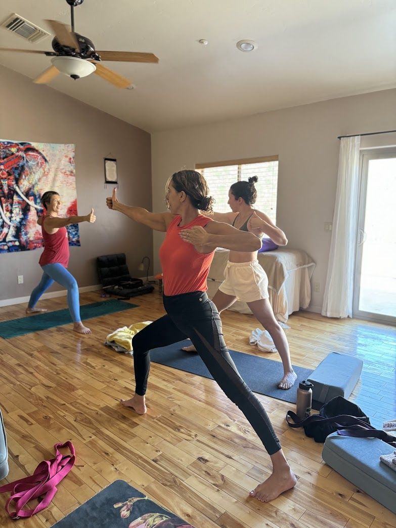 People in yoga poses indoors. One points forward, others stretch arms.