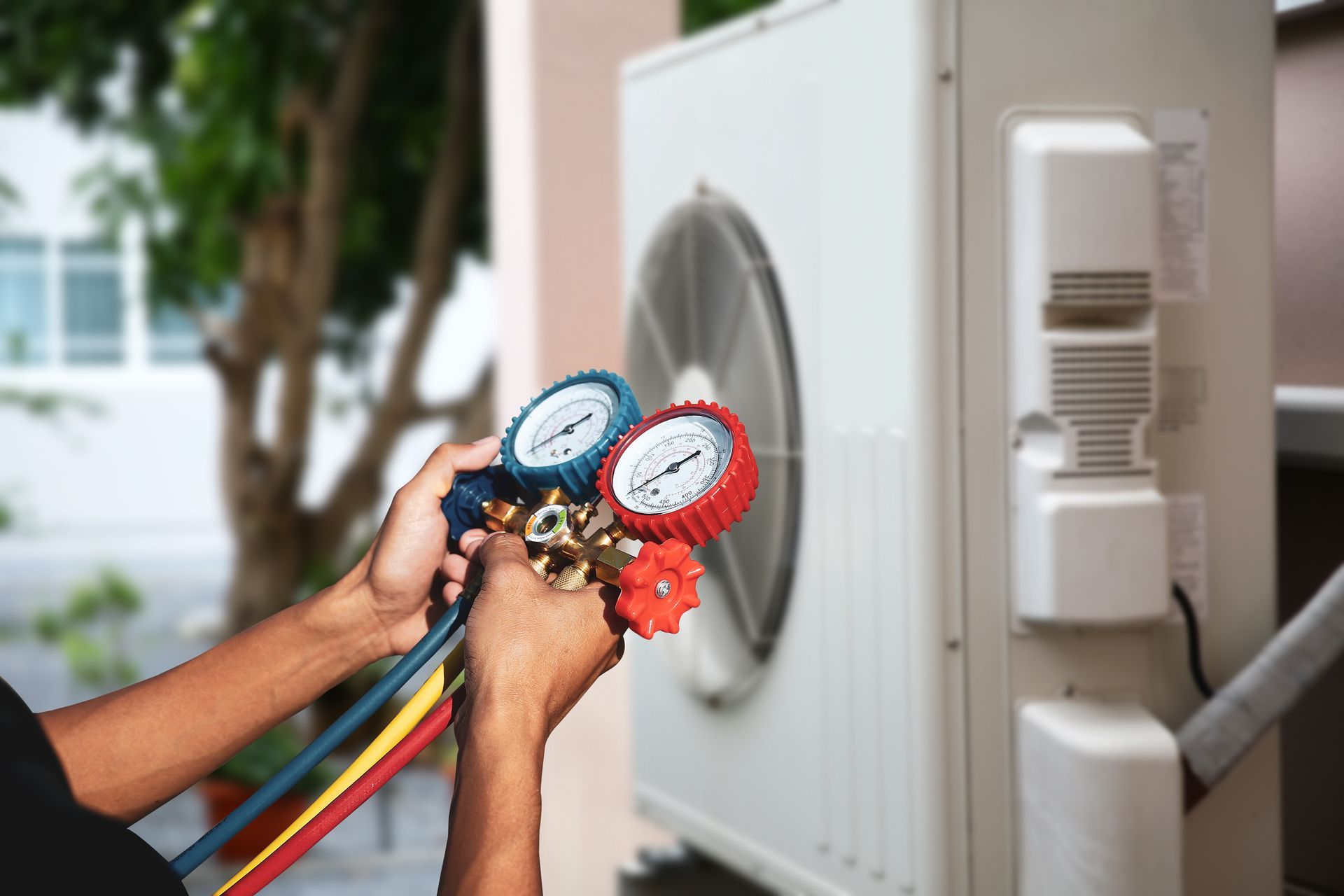 Person holding gauges connecting to an outdoor air conditioner unit.