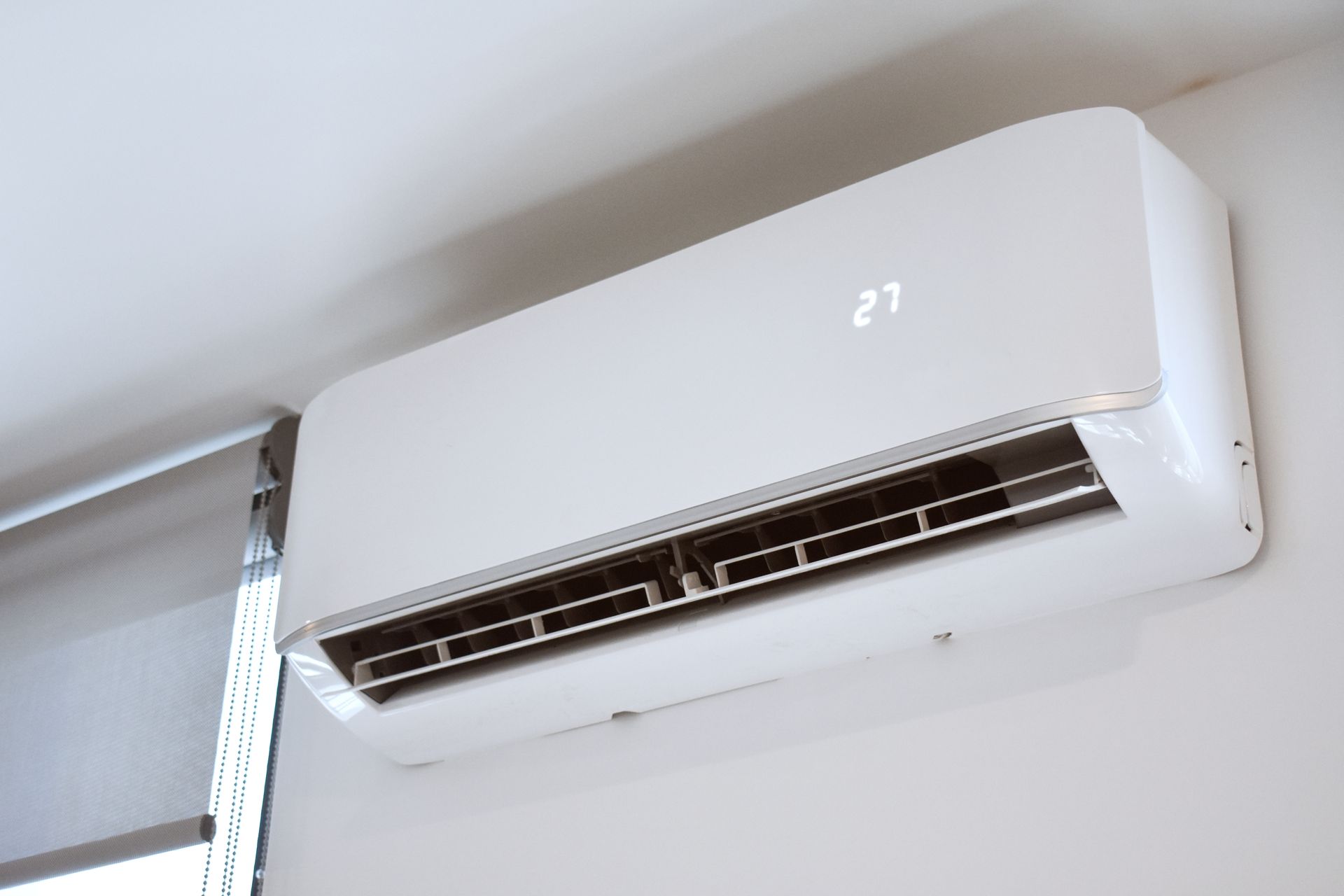 White wall-mounted air conditioner unit showing the set temperature (27) against a white wall.