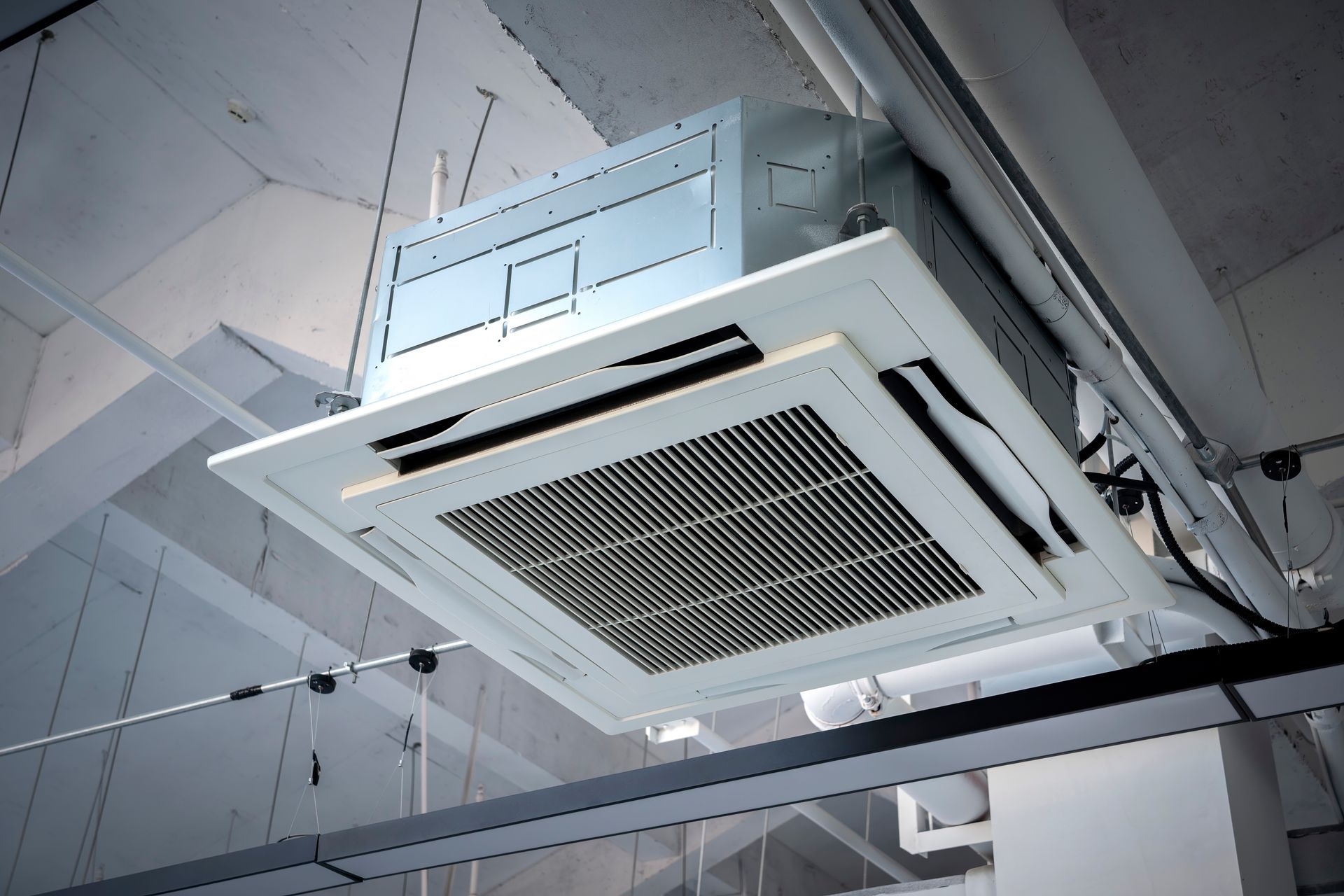 Ceiling-mounted air conditioning unit with a white, grid-like vent. Black trim, installed in a modern building.