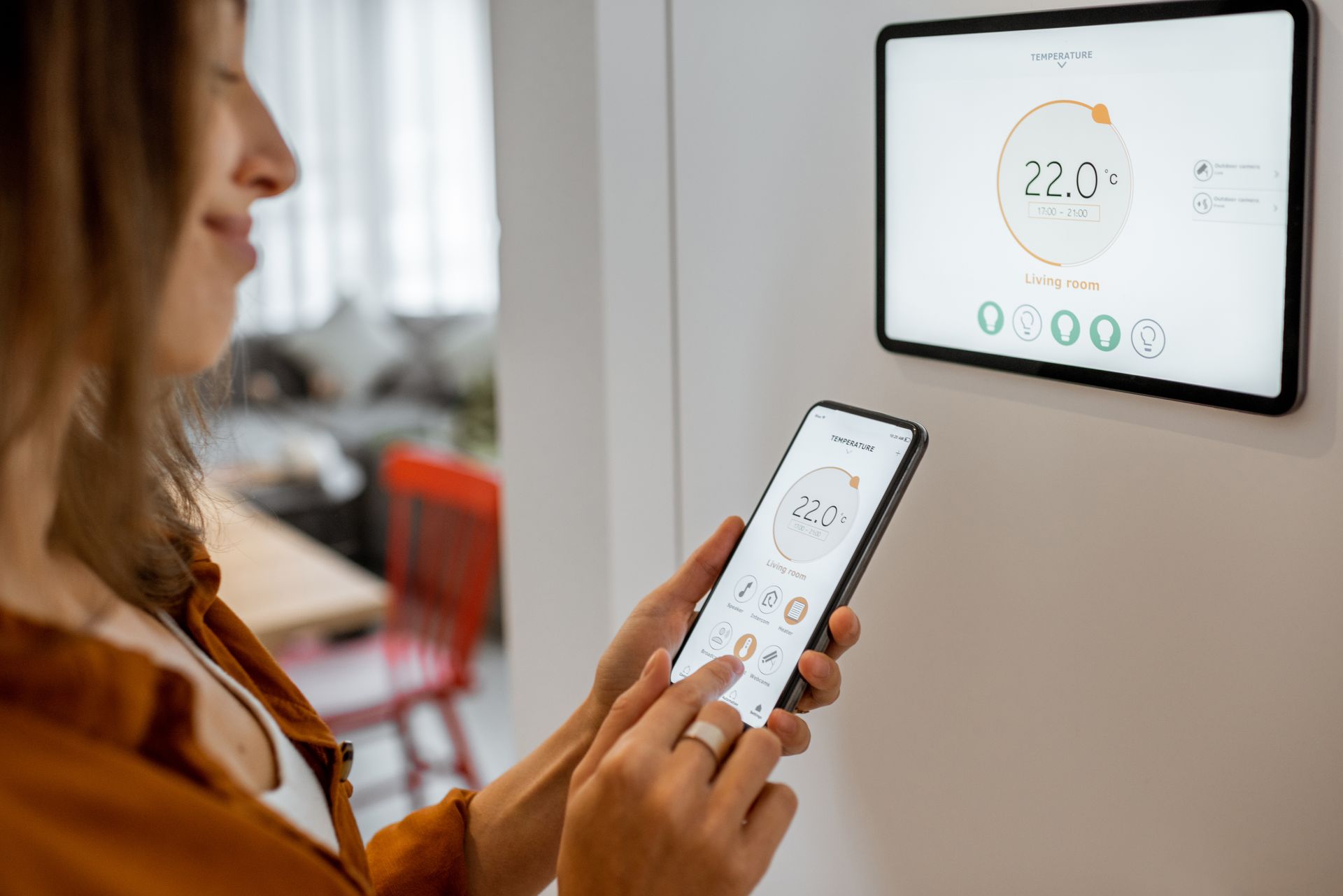 Woman using phone to control smart thermostat; setting room temperature.