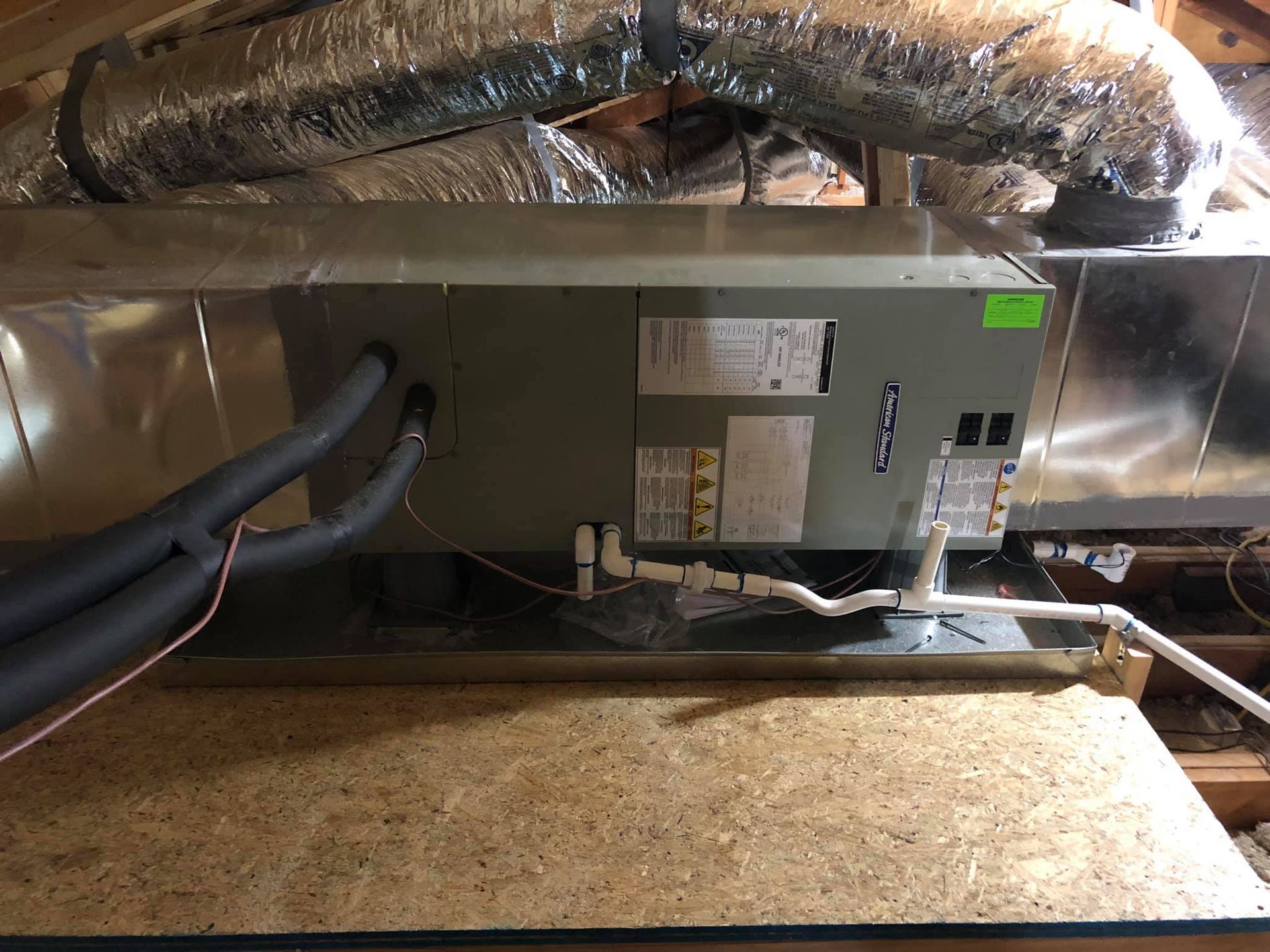 HVAC unit in an attic with ductwork and insulated pipes.