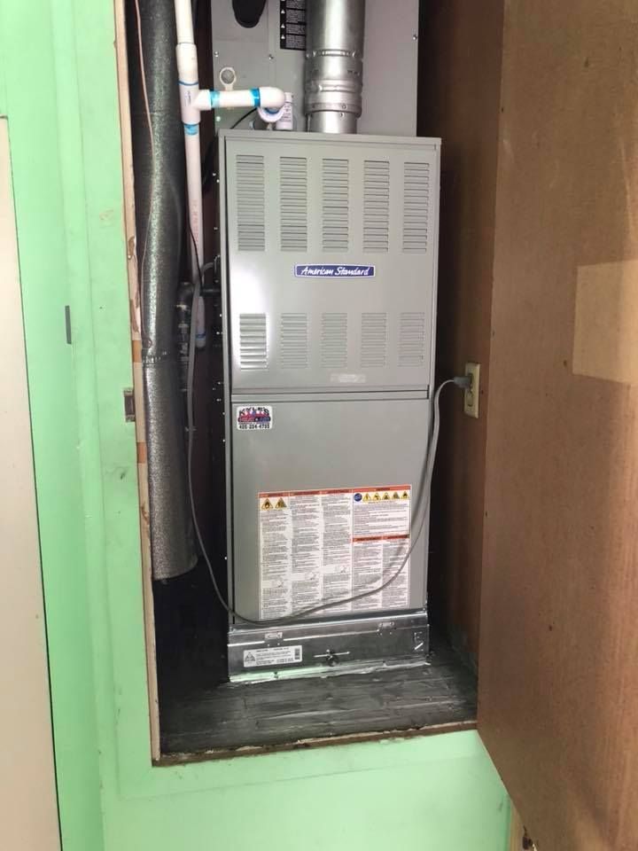 Furnace in a utility closet with vent and gas lines, silver, gray, and white.