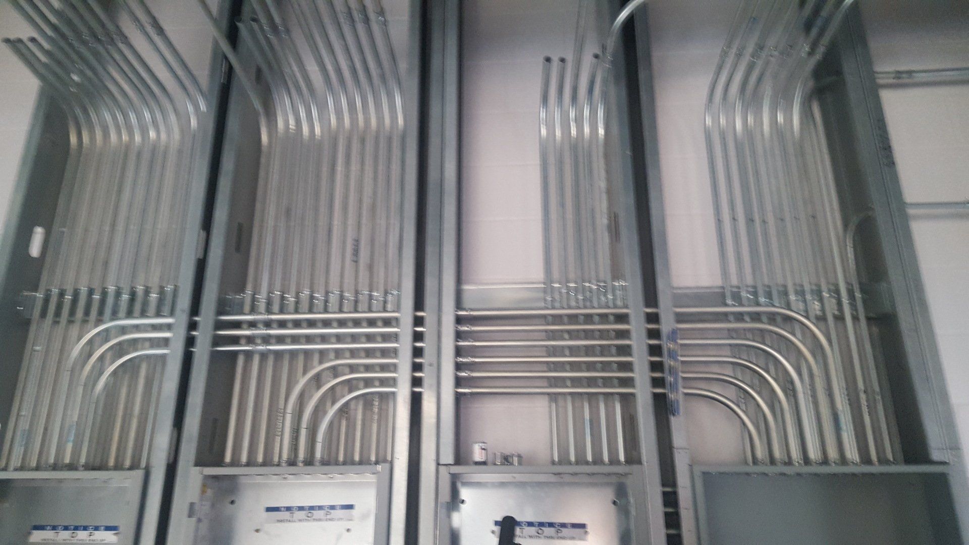 Metal electrical conduits, arranged vertically and horizontally, within a wall frame.