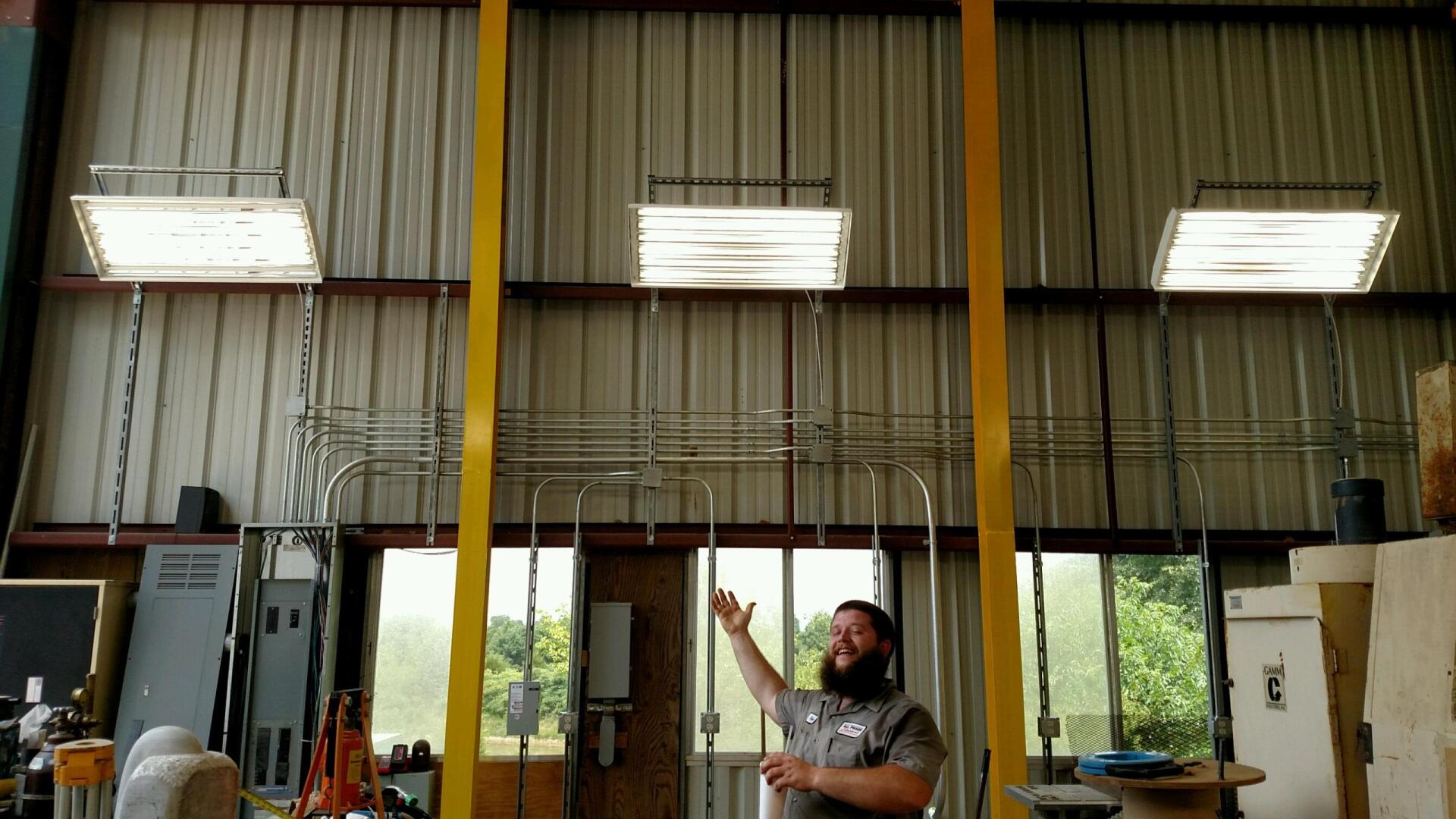 Man pointing up near yellow beams, under fluorescent lights in workshop.