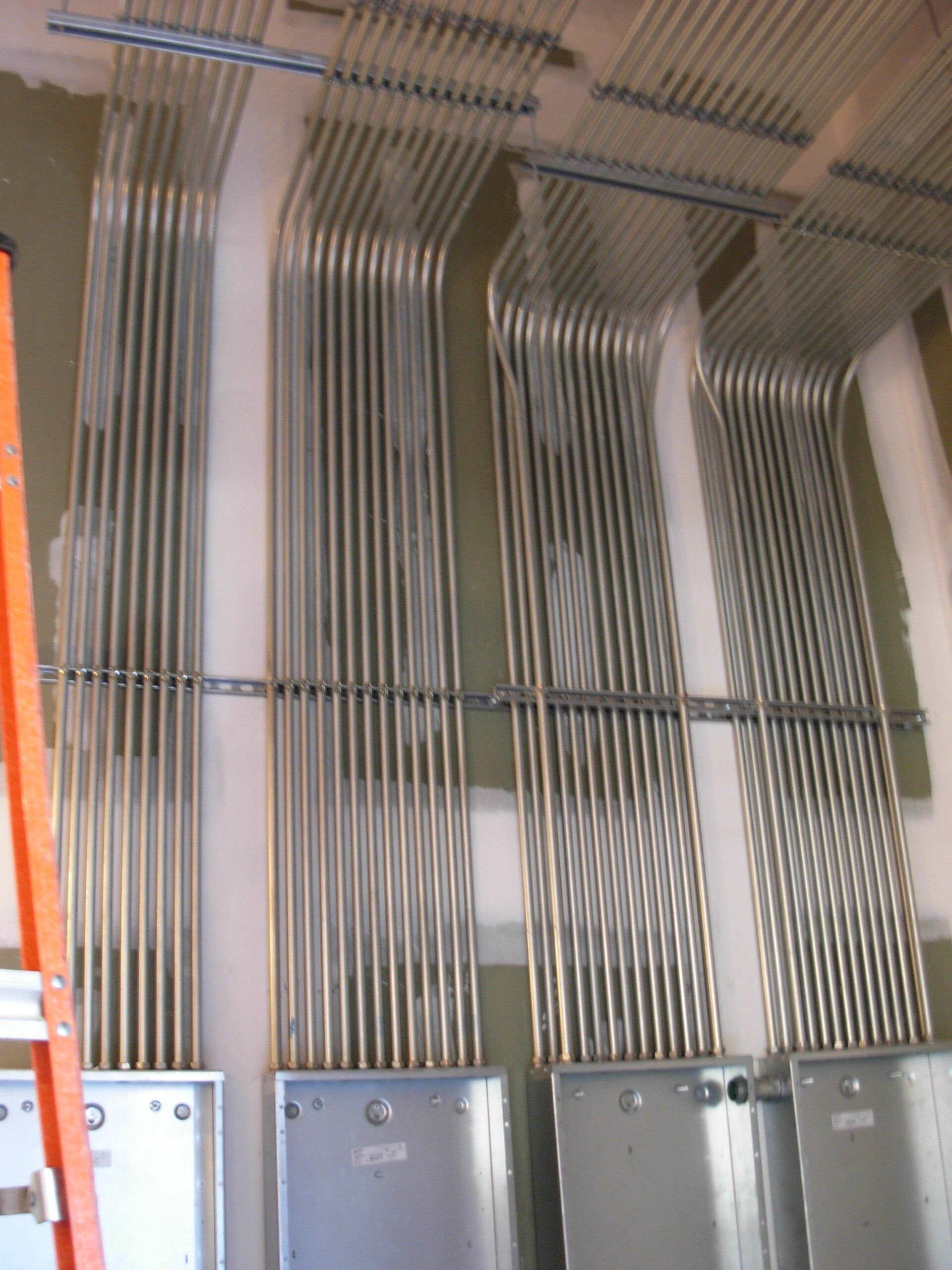 Electrical conduit pipes running vertically, organized, and secured to a wall, connected to gray electrical boxes.