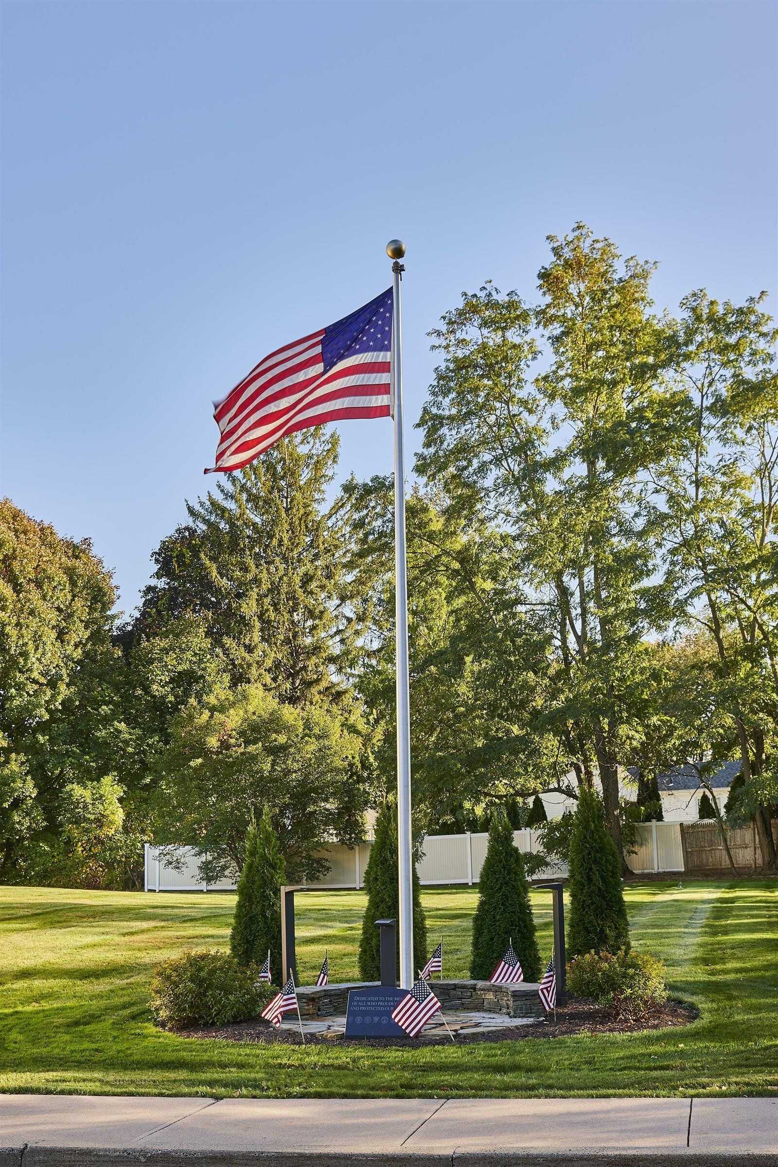 An american flag is flying on a pole in a park.