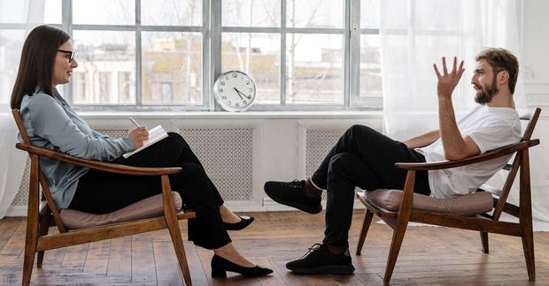 A man and a woman are sitting in chairs talking to each other.
