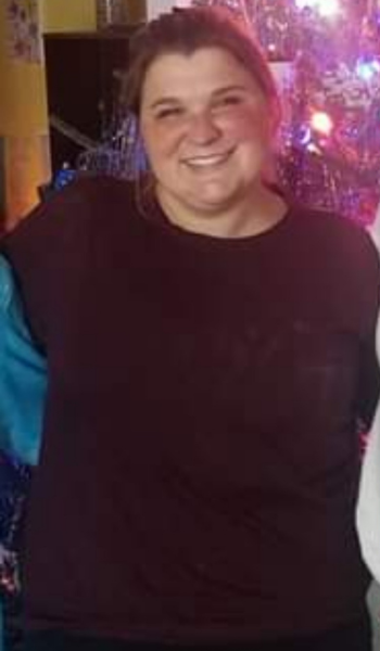 A woman in a black shirt is smiling in front of a christmas tree.