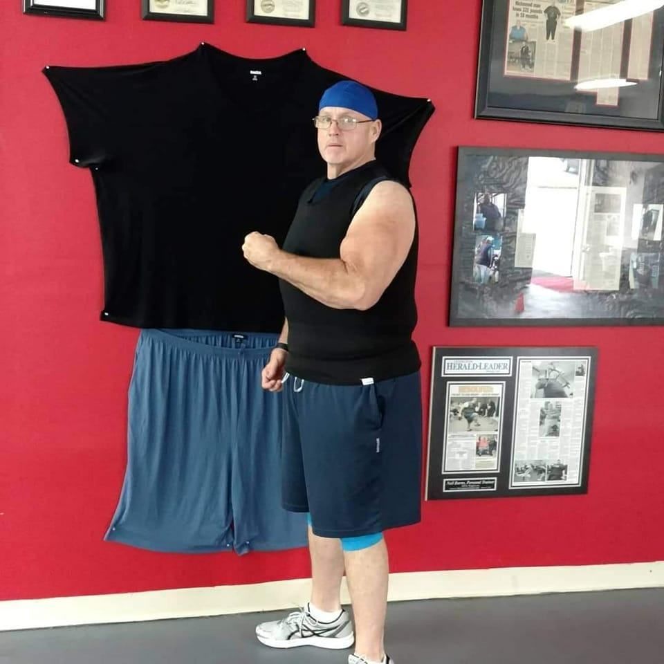 A man is standing in front of a red wall with shirts and shorts hanging on it
