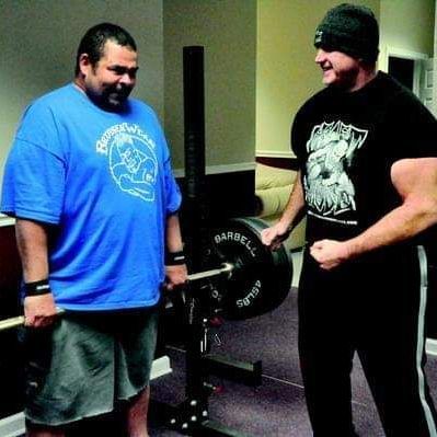 Two men are standing next to each other and one has a shirt that says barbell on it