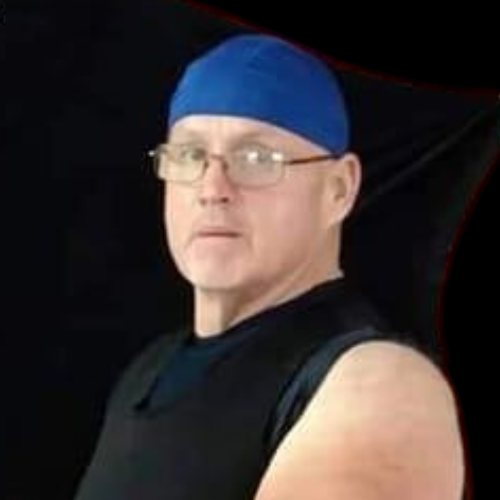 A man wearing glasses and a blue hat is standing in front of a black background.