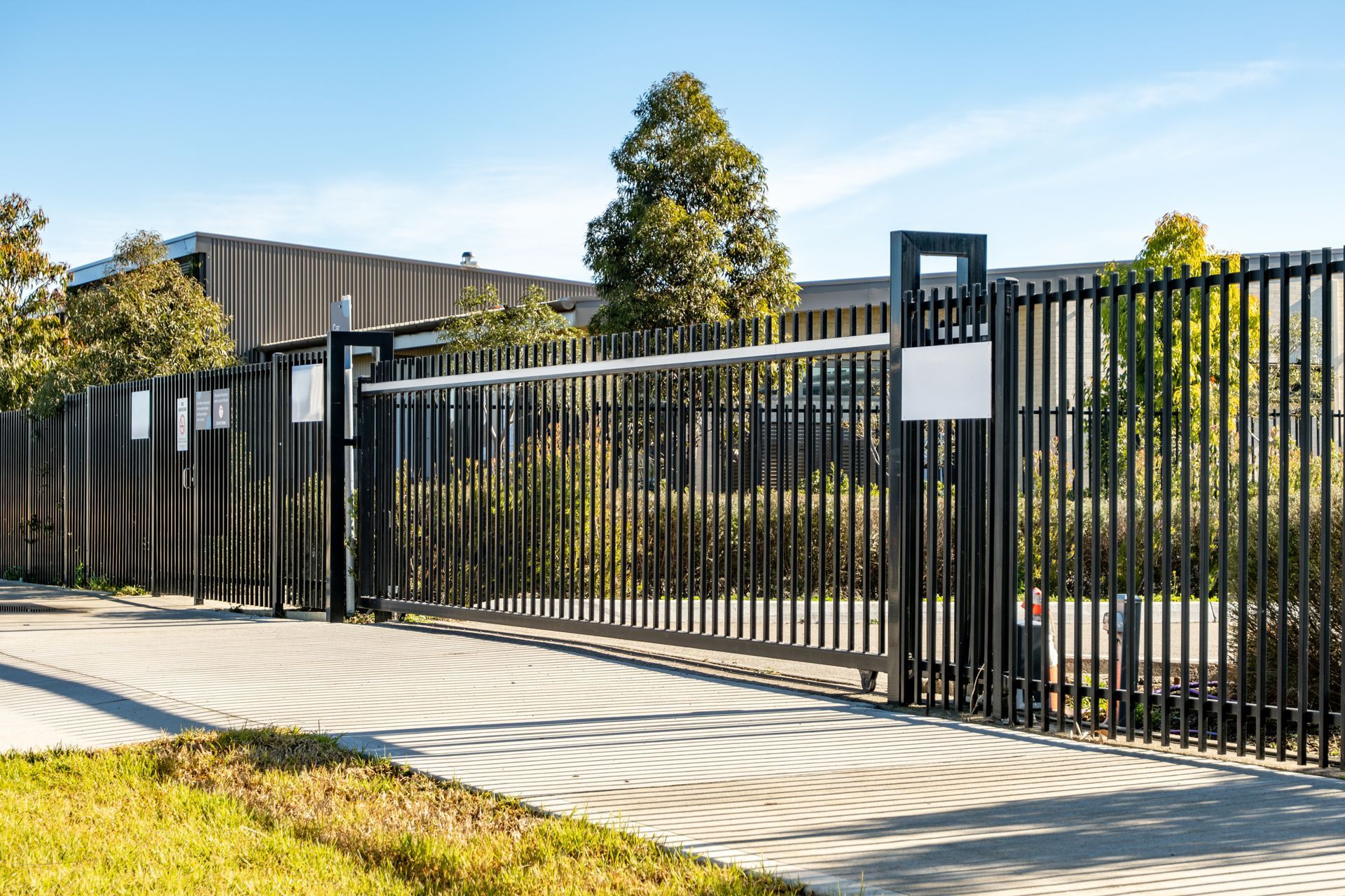 Black metal fence beside a sidewalk and landscaped yard under bright sunlight