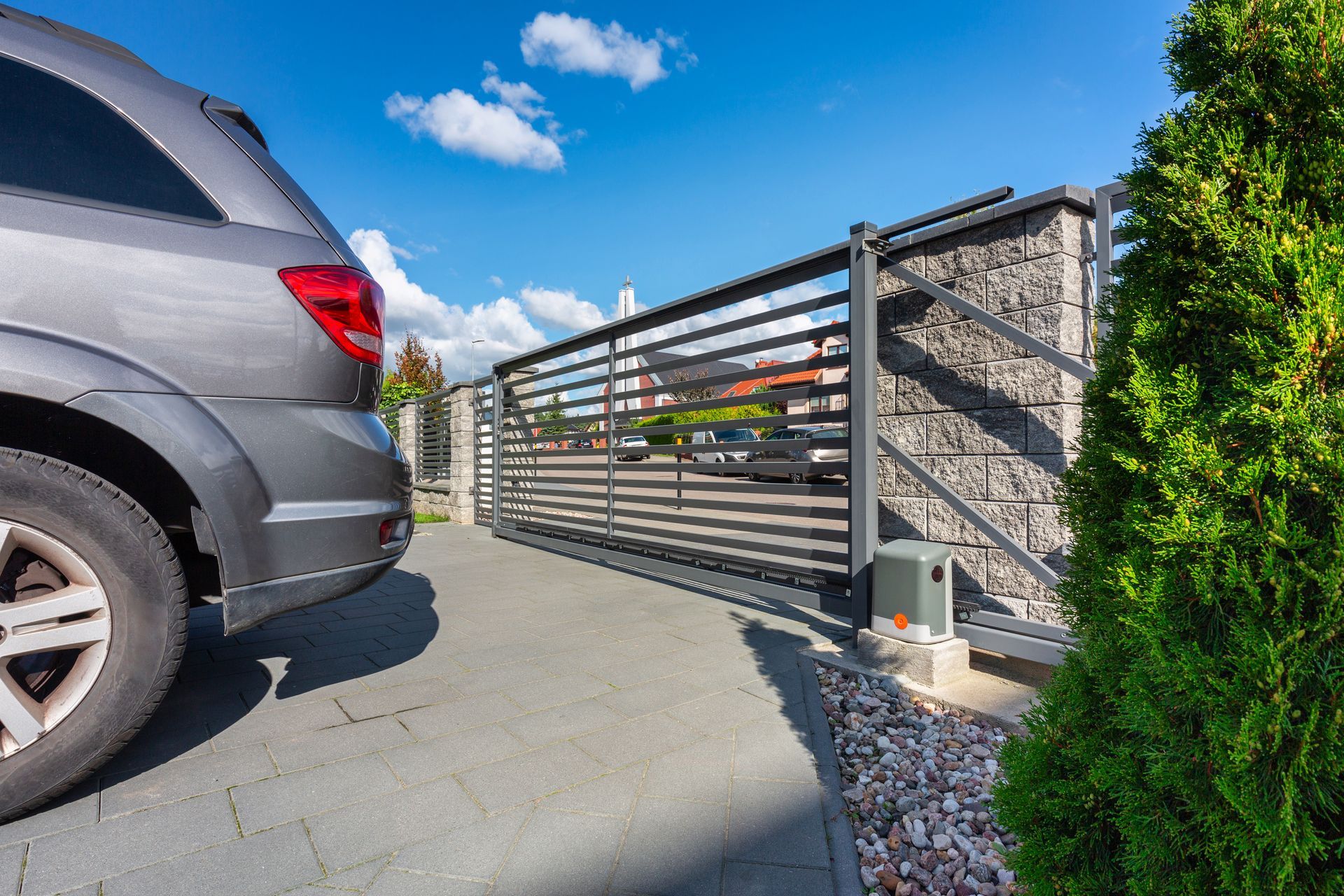 Gray SUV beside a modern metal driveway gate under a blue sky Gray SUV beside a modern metal driveway gate under a blue sky