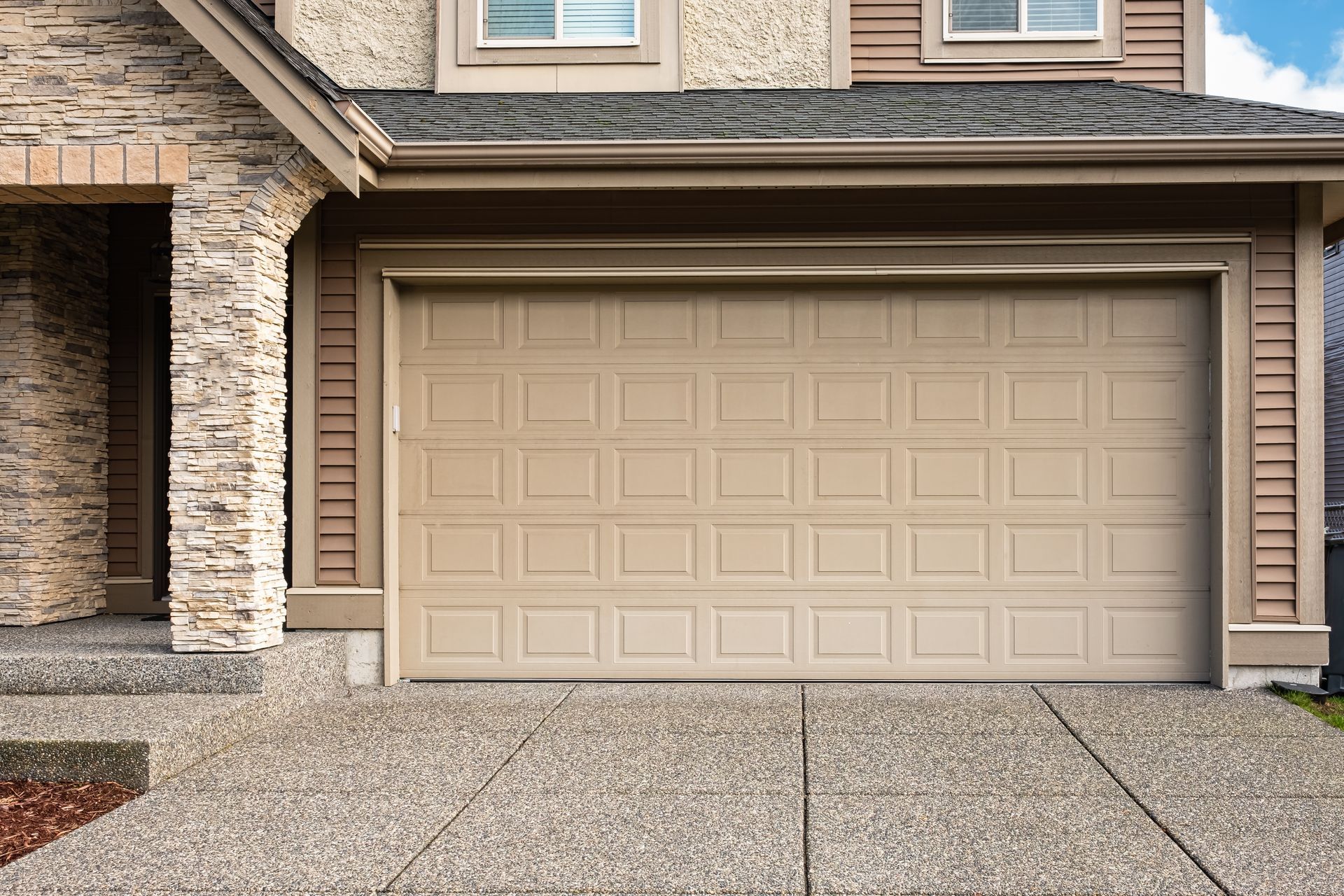 Two-car beige garage attached to a brick-and-siding suburban house with a concrete driveway