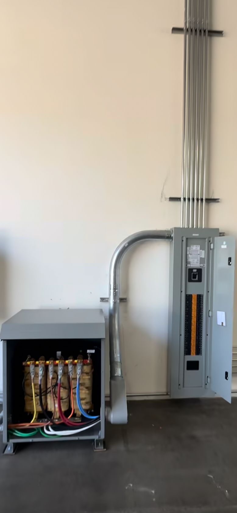 Electrical equipment, including a transformer in an open metal enclosure, connected to a metal electrical panel.