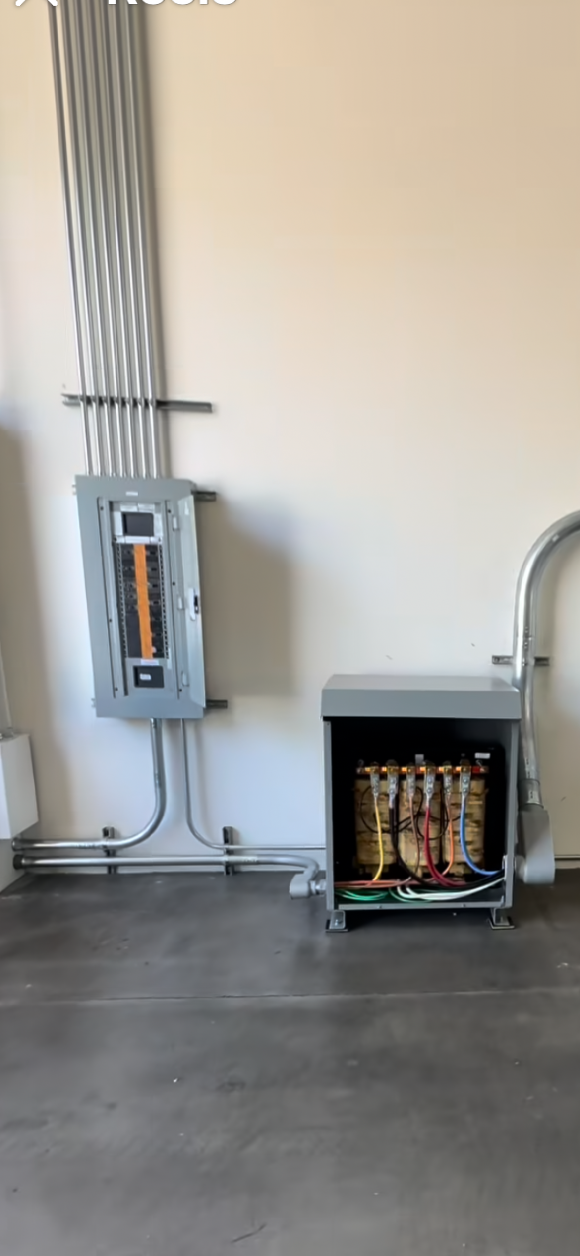 Electrical panel and transformer in a room with concrete flooring and beige walls.